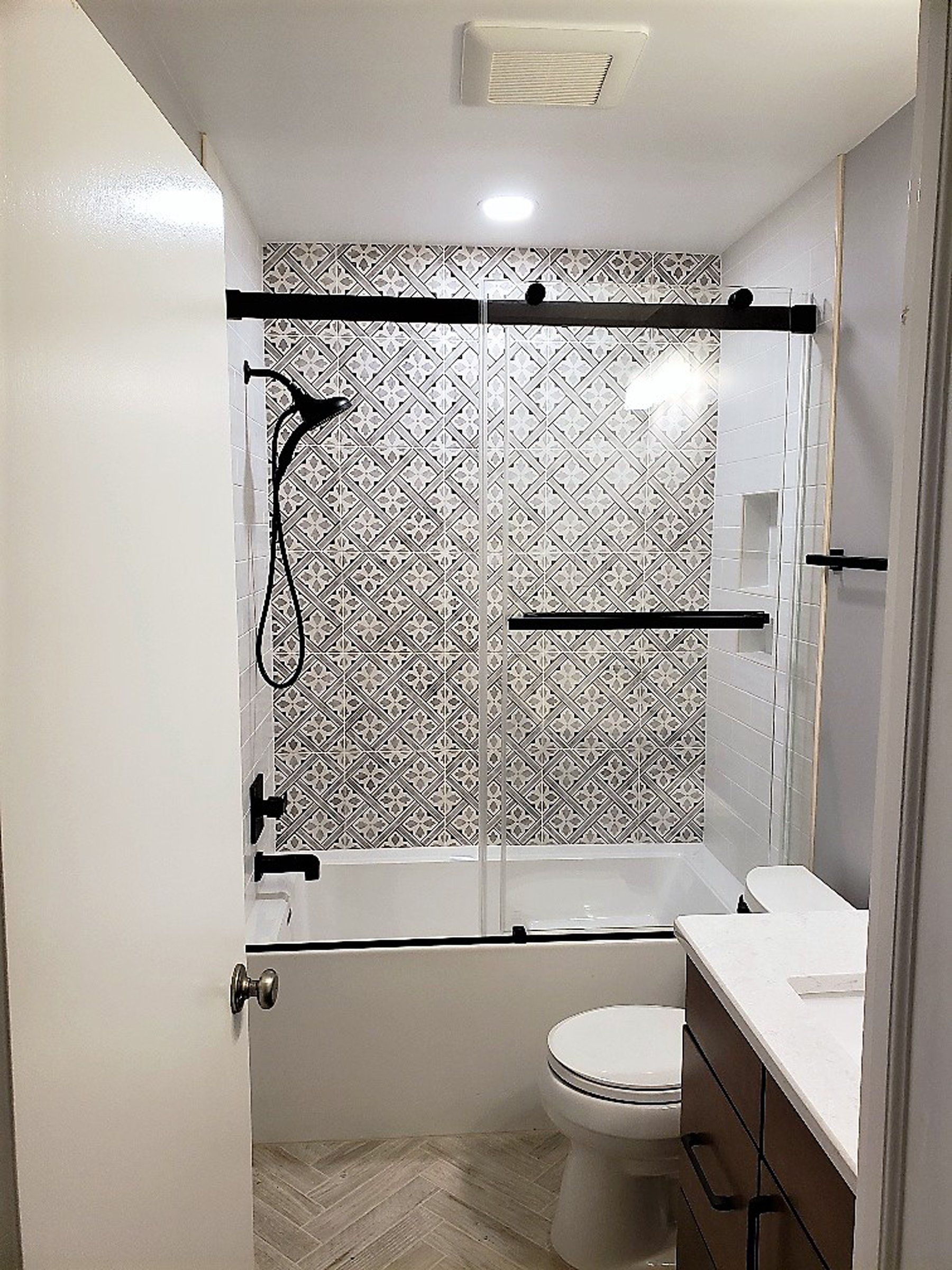 Narrow bathroom with tub-shower, patterned tile, toilet, and vanity sink  in Rockville
