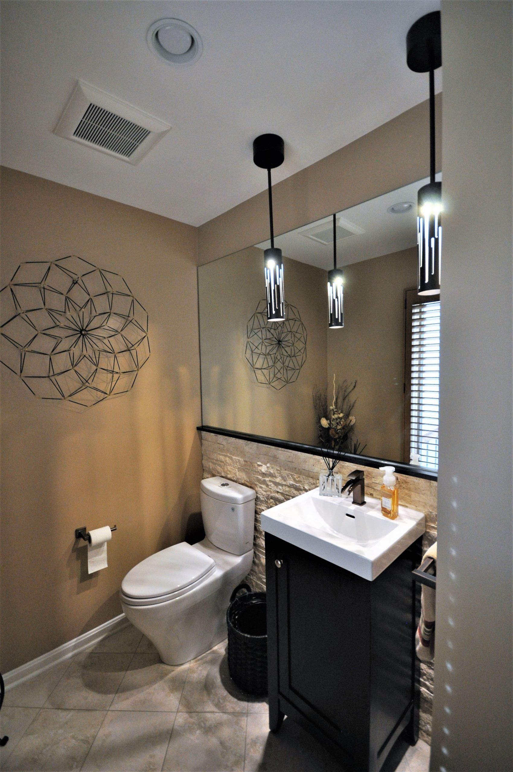 Small beige bathroom with toilet, vanity sink, mirror, and pendant lights in Brookeville