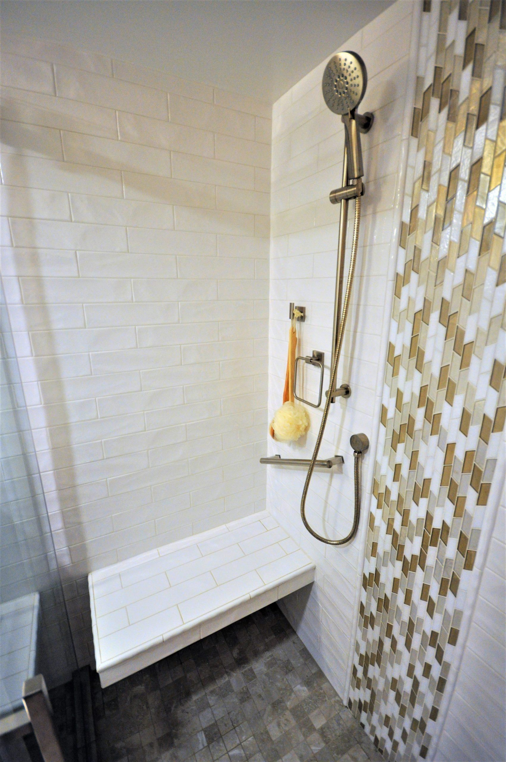 Modern shower with white bench, handheld showerhead, and gold-and-white mosaic tile wall in Derwood