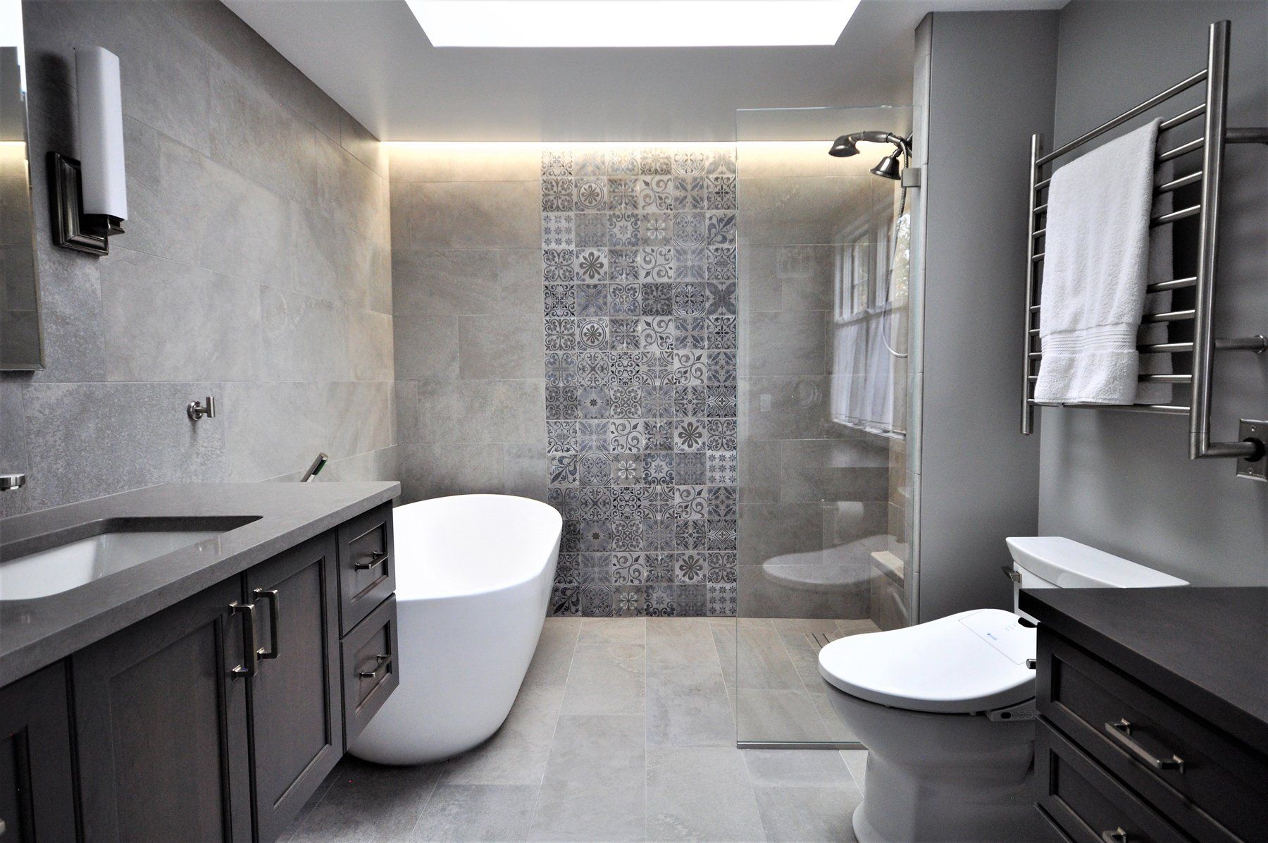 Modern gray bathroom with freestanding tub, tiled shower, dark vanity, and towel rack  in Rockville