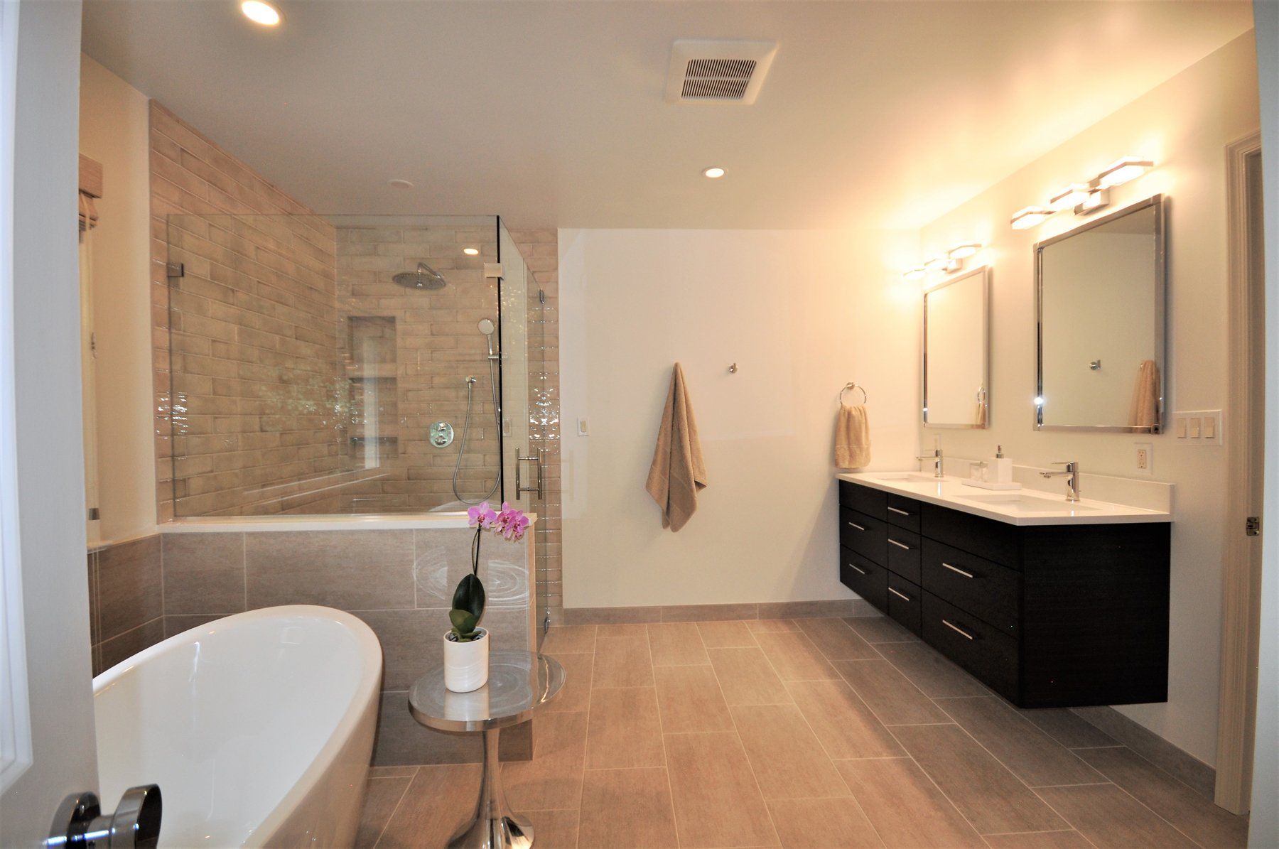 Modern bathroom with freestanding tub, glass shower, double vanity, and warm wood flooring  in Rockville