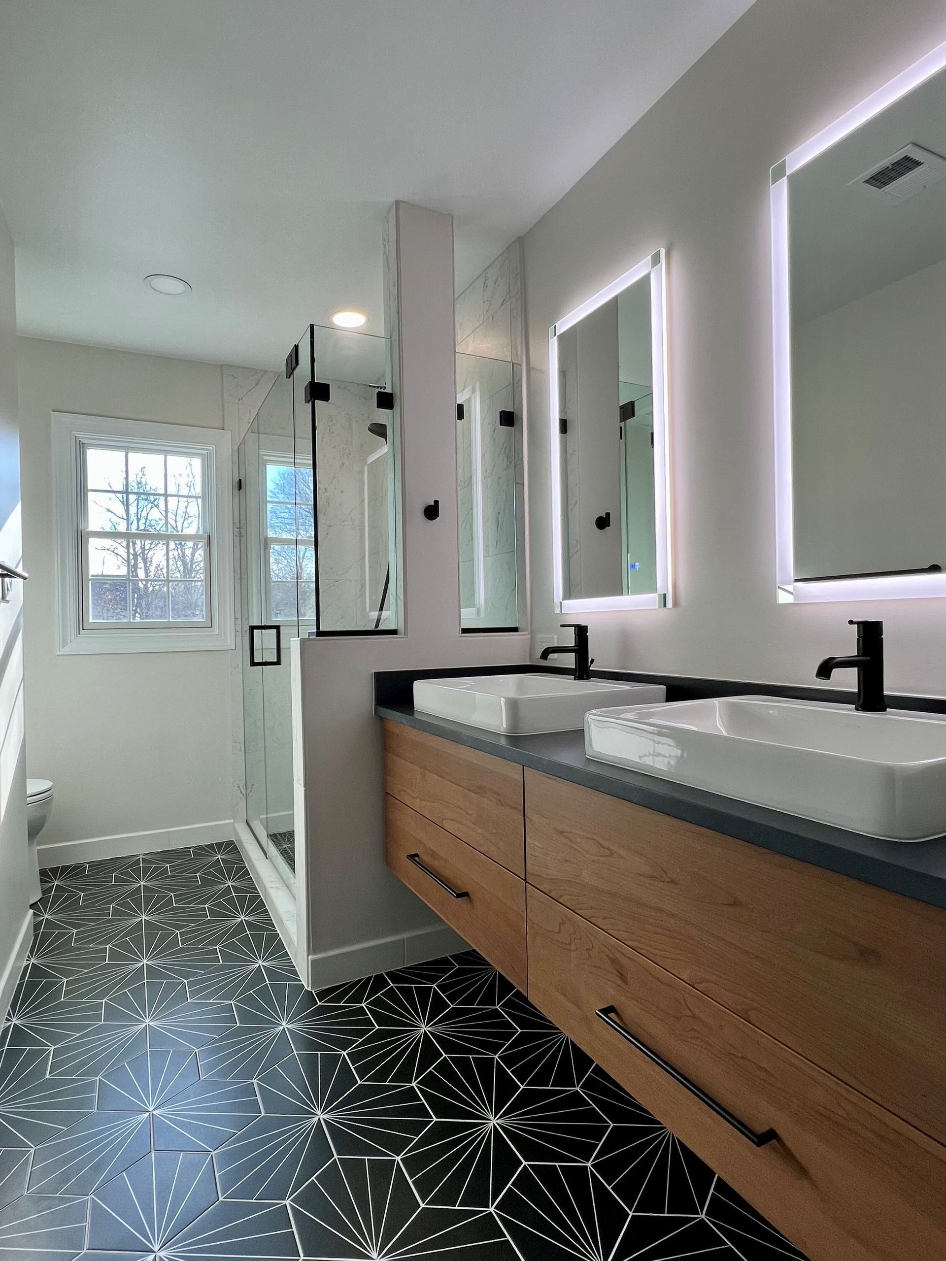 Modern bathroom with double sink vanity, black fixtures, wood cabinets, and patterned black-and-white floor tiles  in Rockville