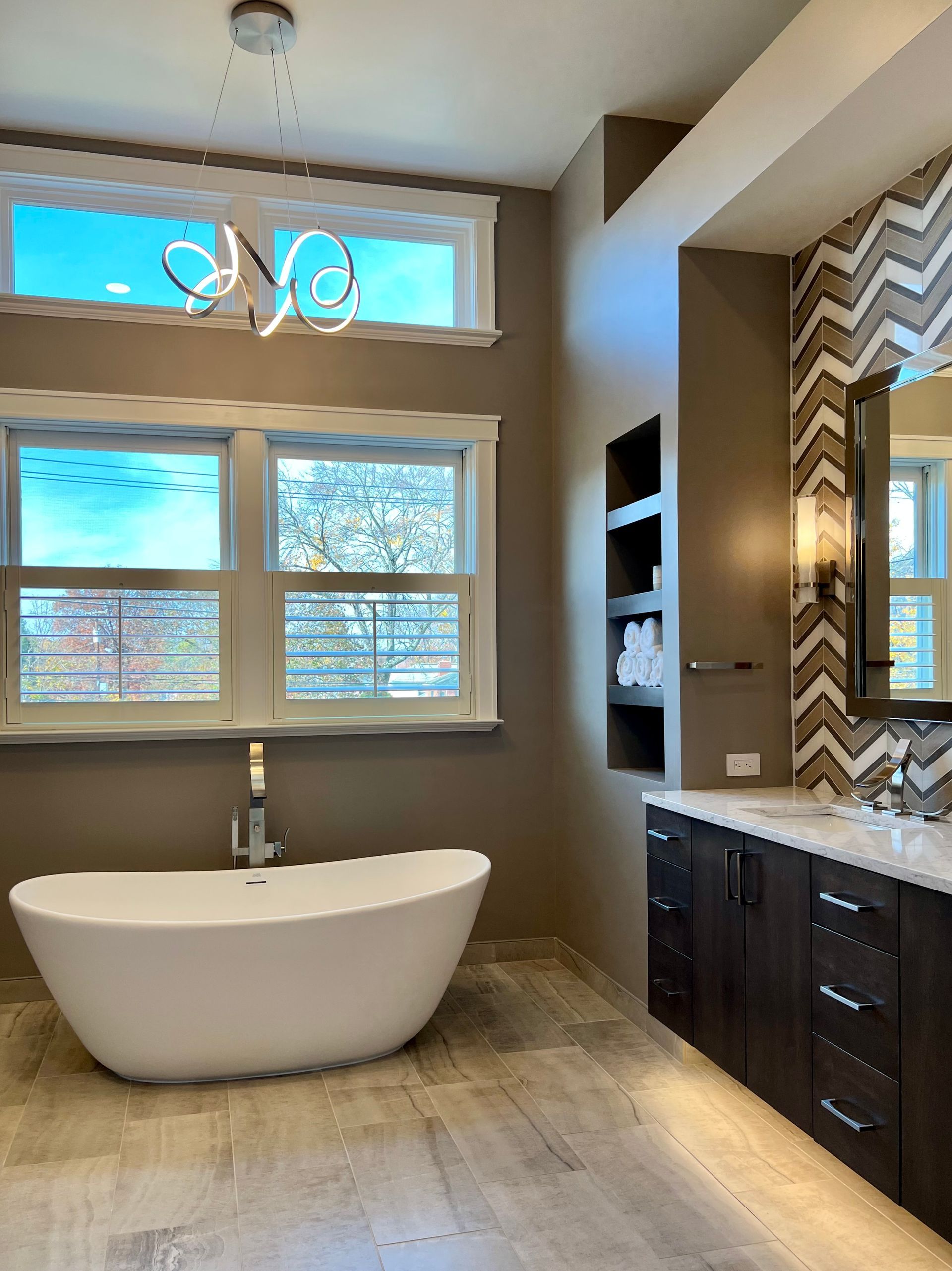 Modern bathroom with freestanding tub, double vanity, large window, and chevron tile accent wall  in Rockville