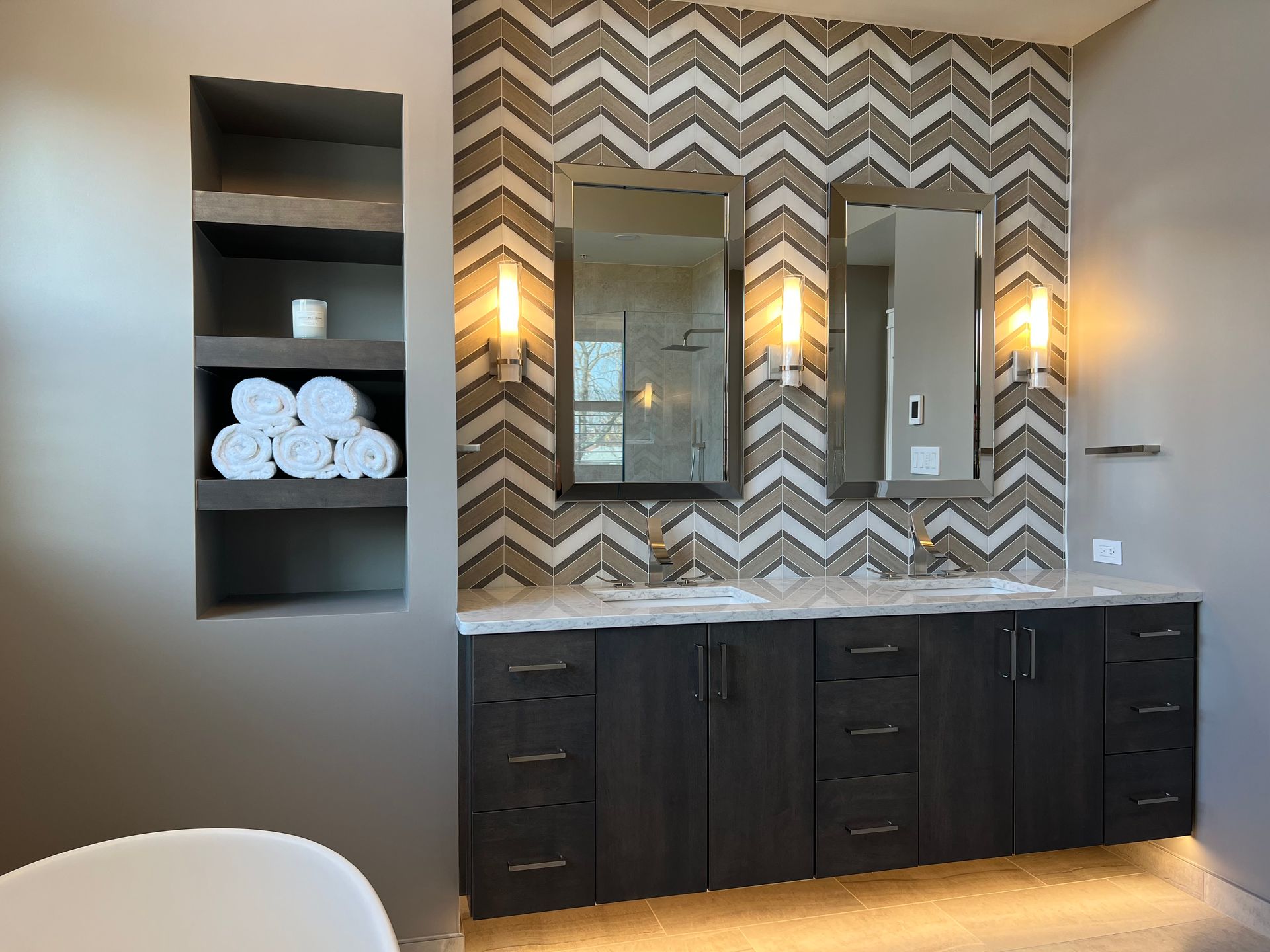 Bathroom vanity with double sinks, dark cabinets, chevron wallpaper, mirrors, and built-in shelves with towels  in Rockville