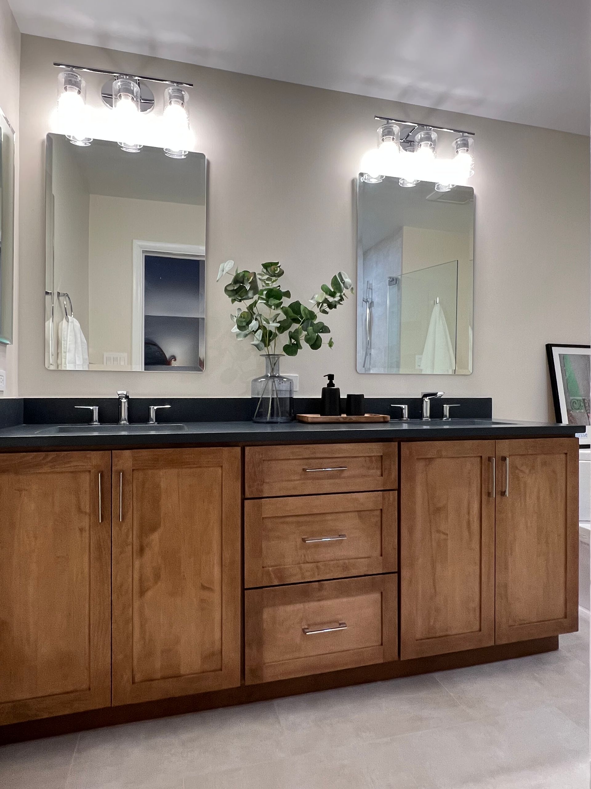 Double-sink bathroom vanity with wood cabinets, black countertop, mirrors, and wall lights  in Rockville