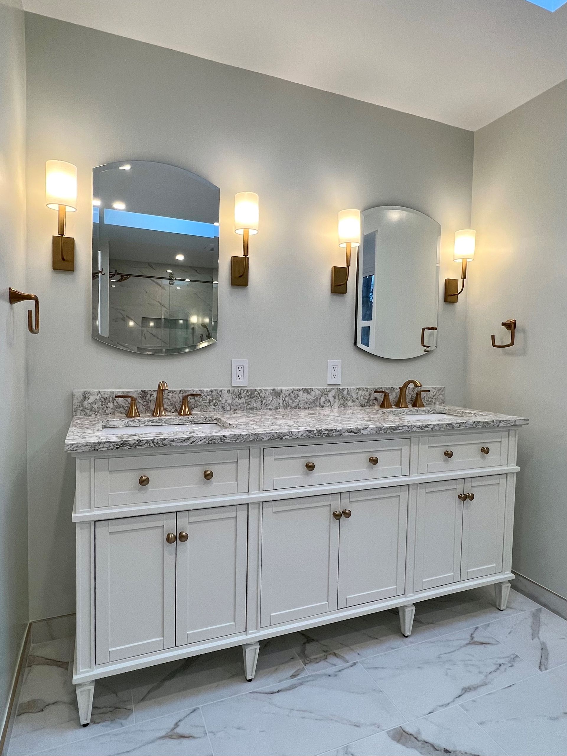 Elegant bathroom vanity with marble countertop, double mirrors, and wall sconces on light gray walls  in Rockville