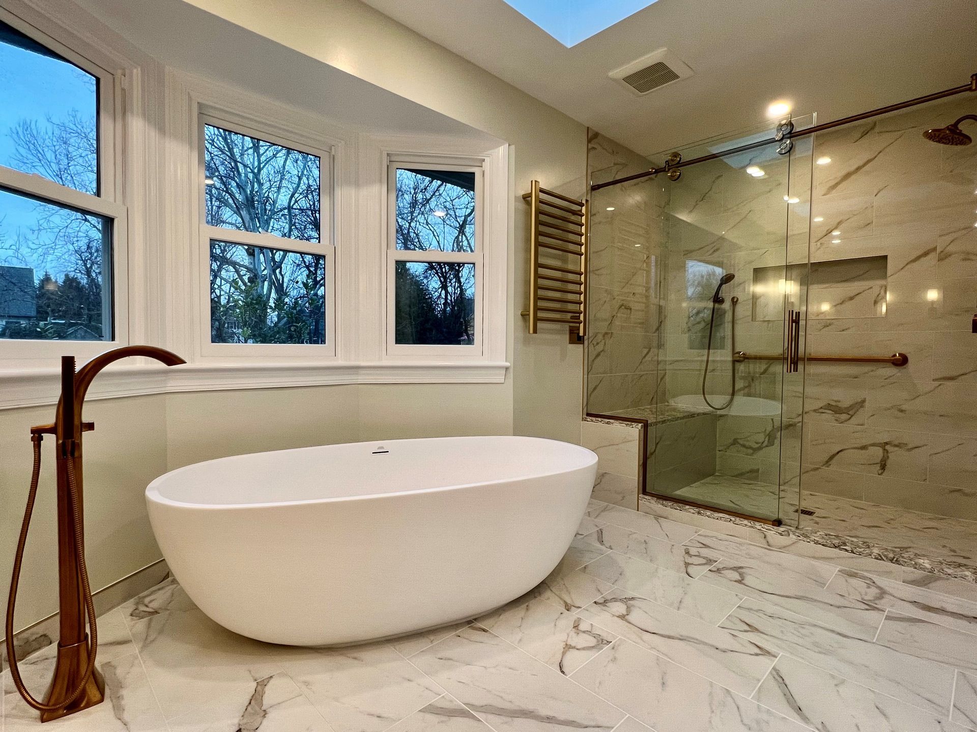 Modern bathroom with freestanding tub, glass shower, marble tile, and large windows  in Rockville