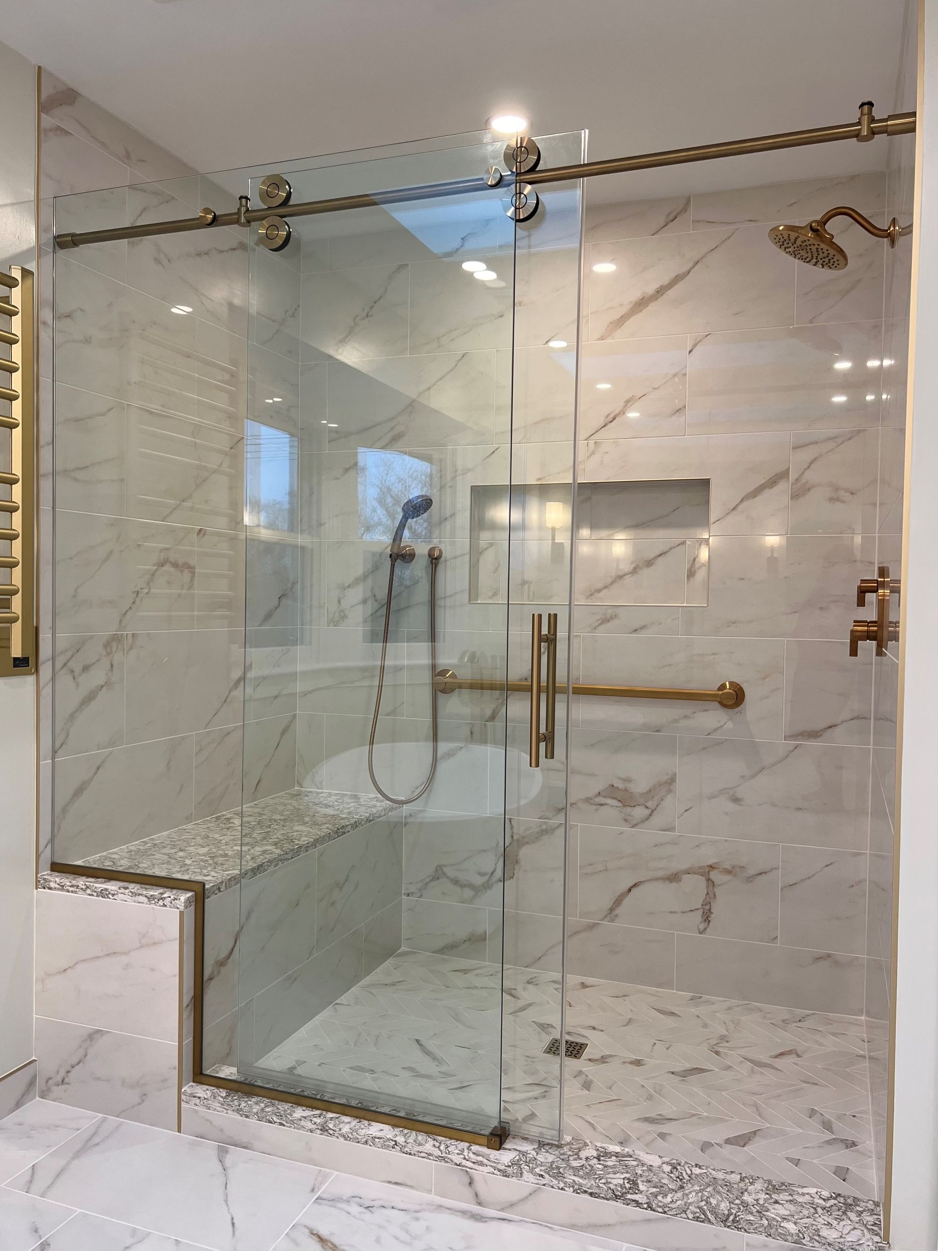 Modern glass shower with marble tile walls and floor, gold fixtures, and built-in bench  in Rockville