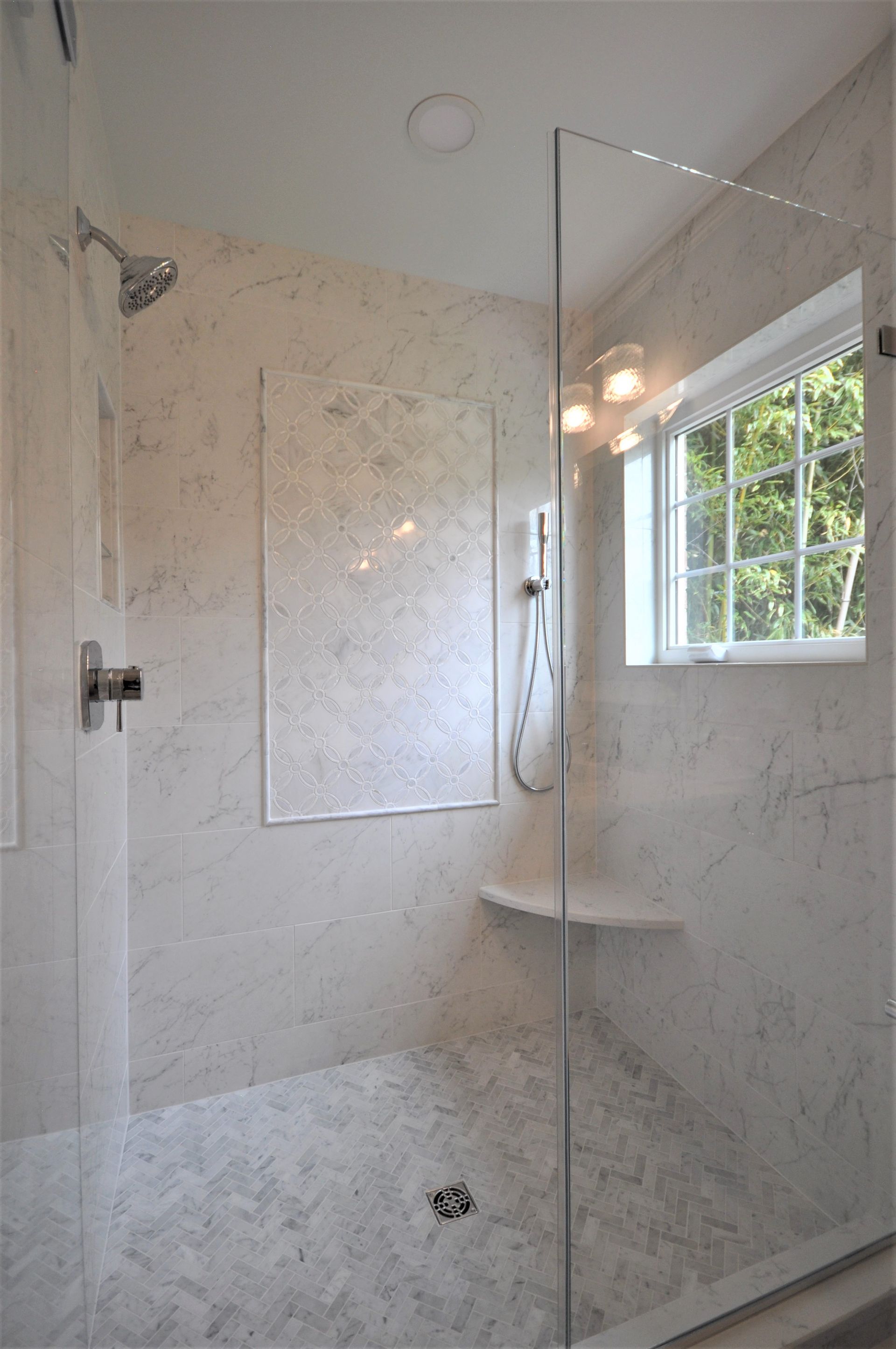 Walk-in shower with marble-look walls, glass partition, handheld showerhead, and a window beside the shower  in Rockville