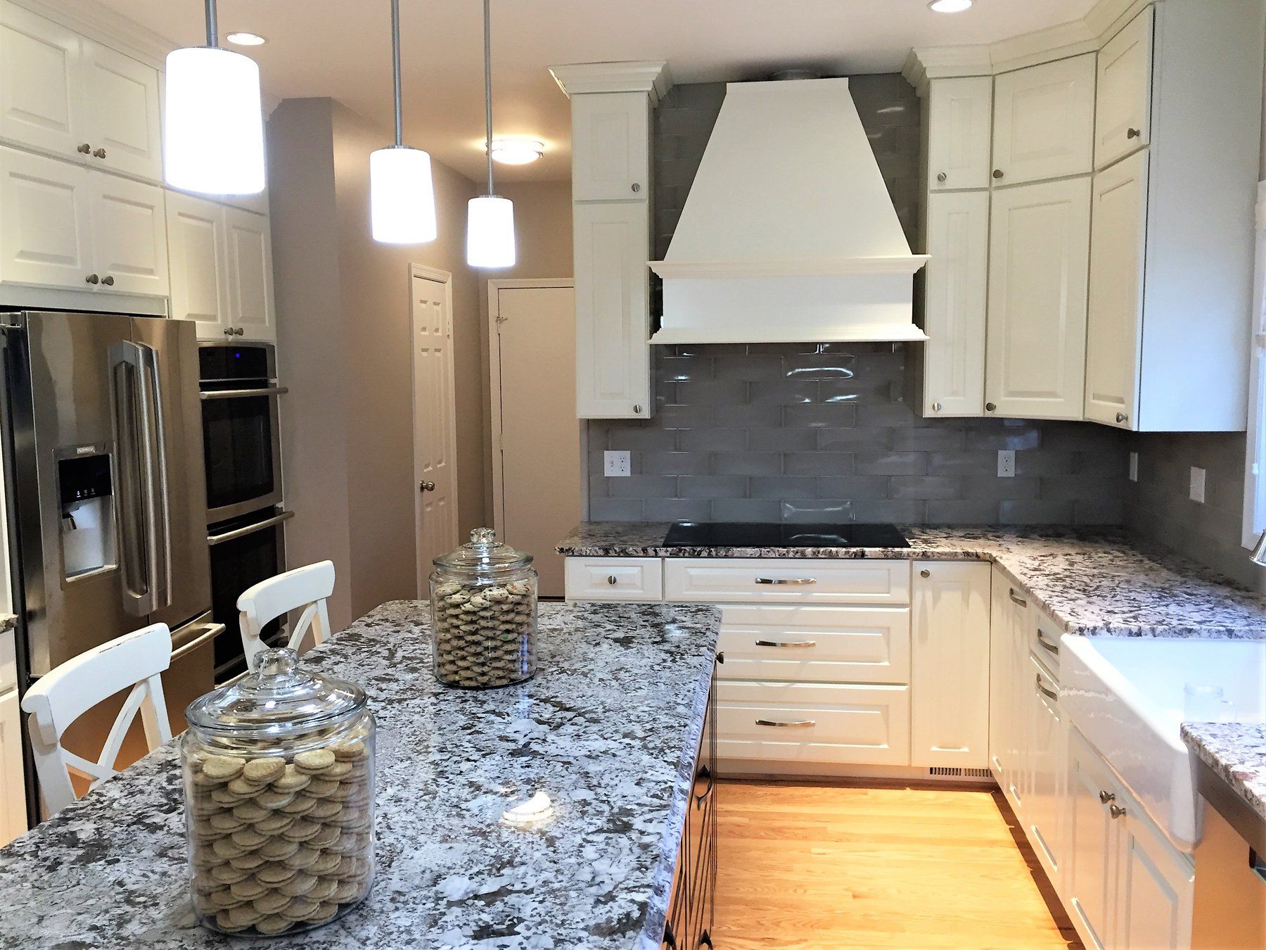 Bright modern kitchen with white cabinets, granite island, stainless appliances, and pendant lights in Bethesda