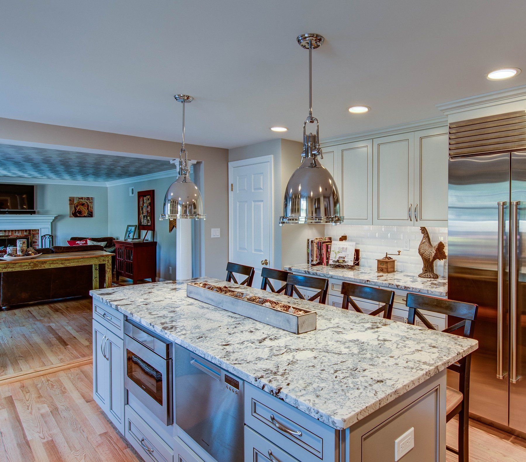 Modern kitchen with granite island, pendant lights, white cabinets, and stainless steel refrigerator in Rockville