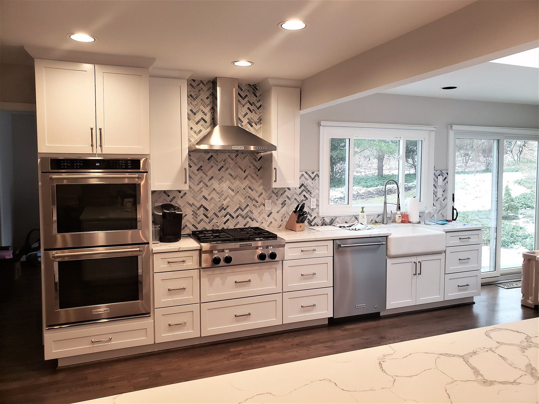 Bright modern kitchen with white cabinets, stainless appliances, marble backsplash, and large windows in Rockville