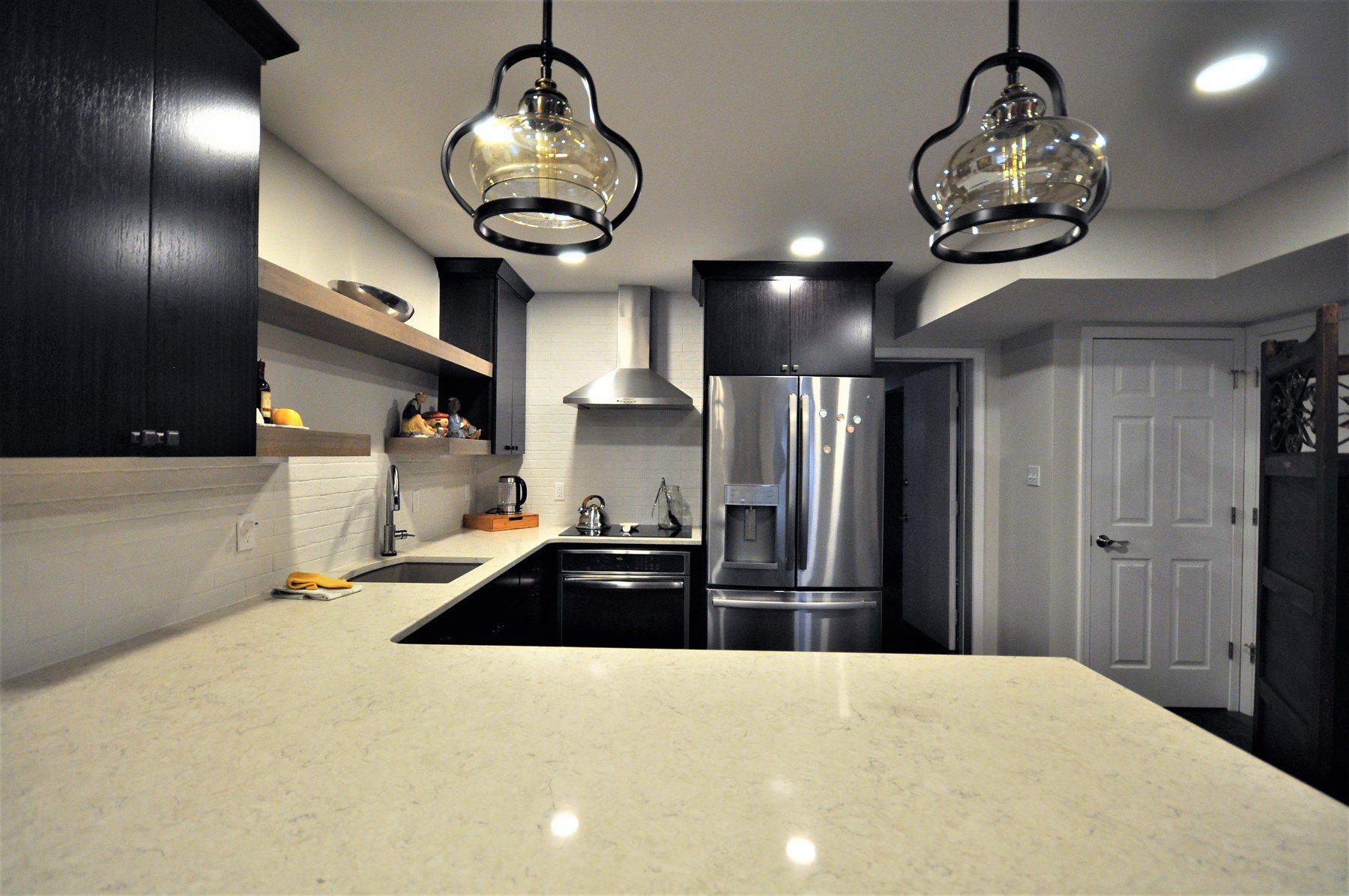 Modern kitchen with black cabinets, stainless steel appliances, and a light countertop beneath pendant lights in Chevy Chase