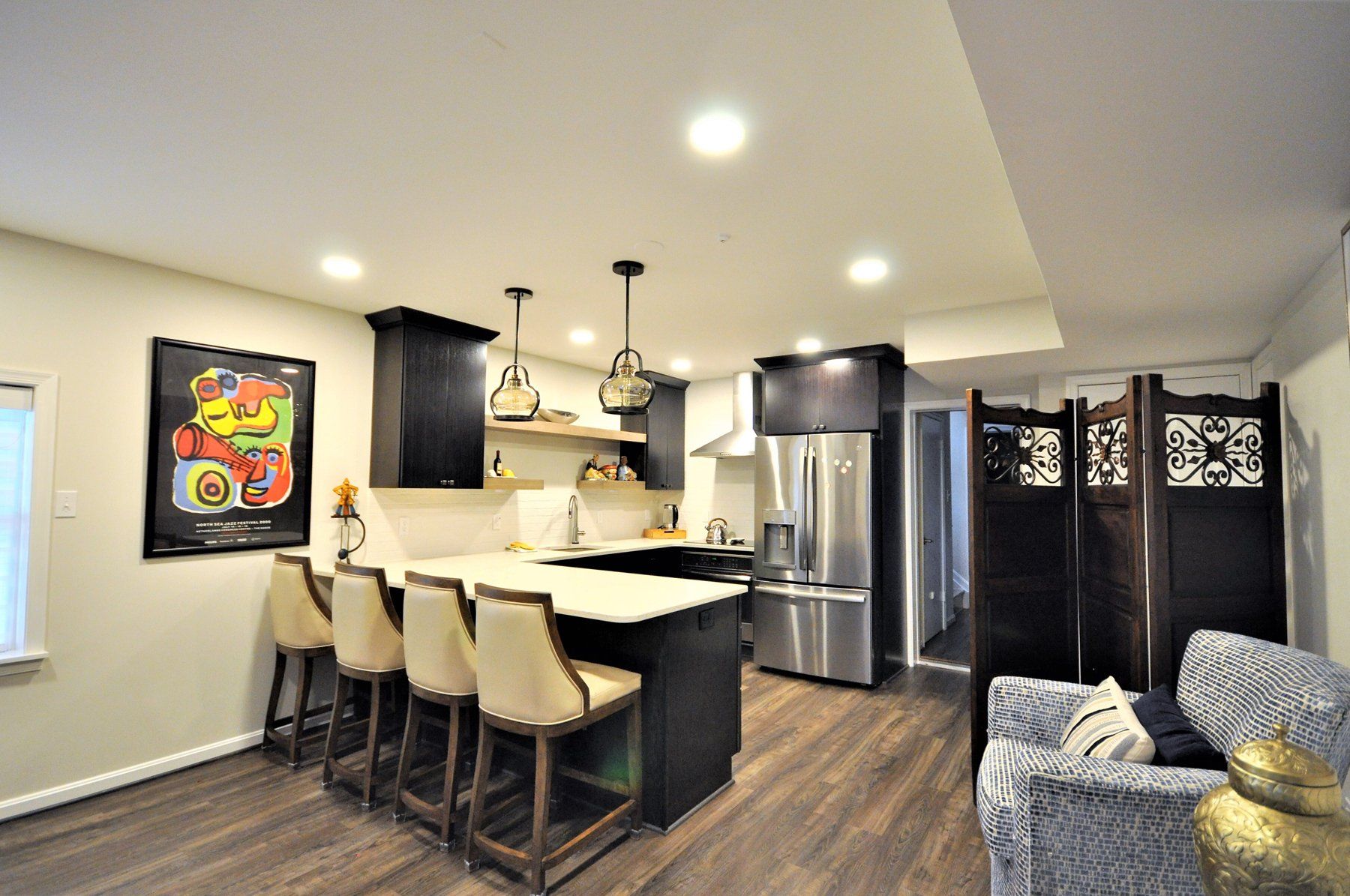 Modern kitchen and dining area with island seating, stainless fridge, dark wood floors, and wall art in Rockville