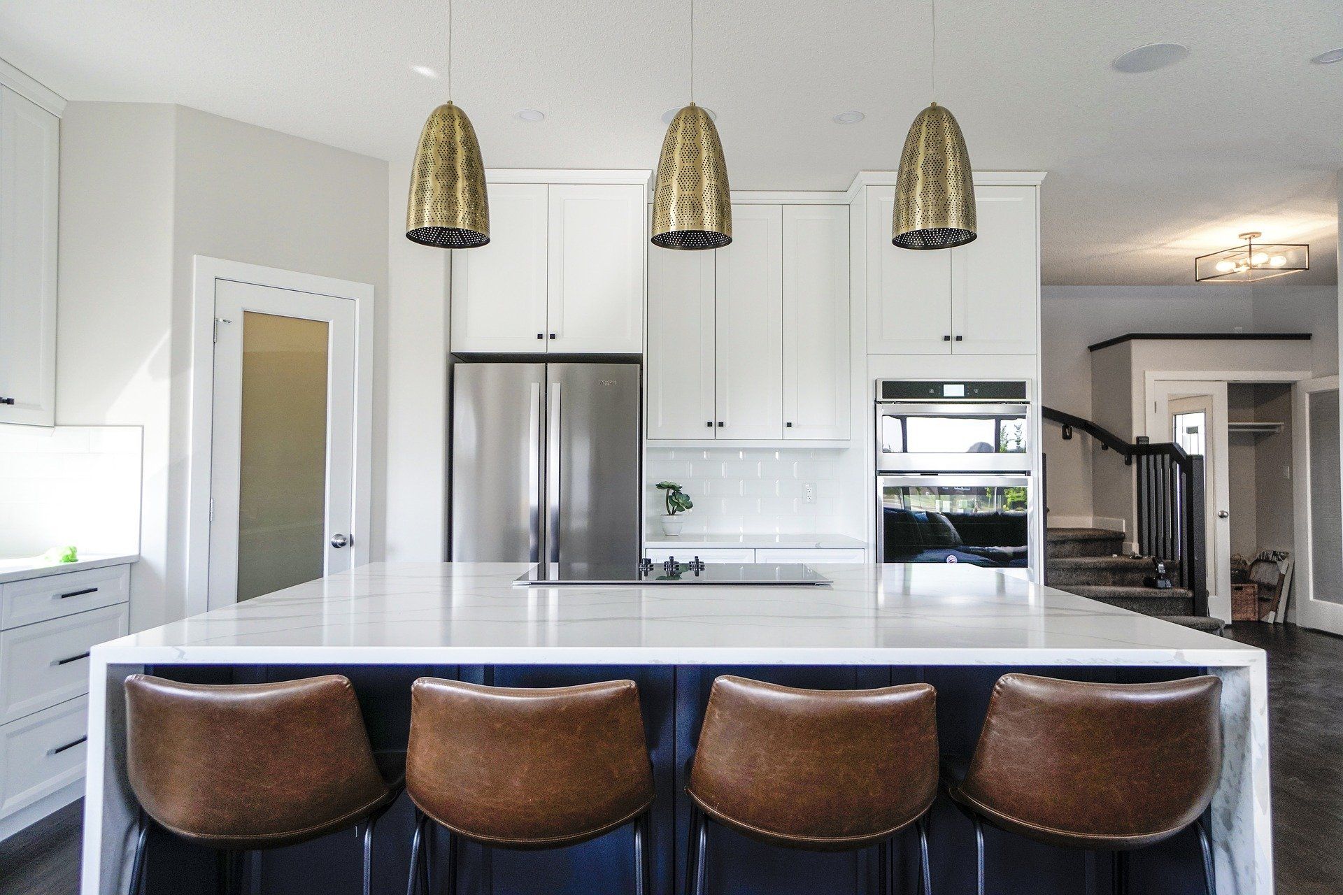 Modern white kitchen with island, stainless steel appliances, and three brown bar stools under pendant lights in Rockville