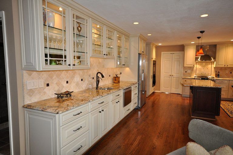 Bright modern kitchen with white cabinets, marble counters, and warm wood floors, open to a living area in Rockville