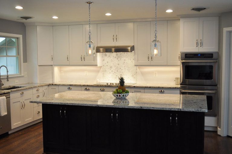 Modern white kitchen with granite island, pendant lights, and built-in stainless steel oven in Rockville