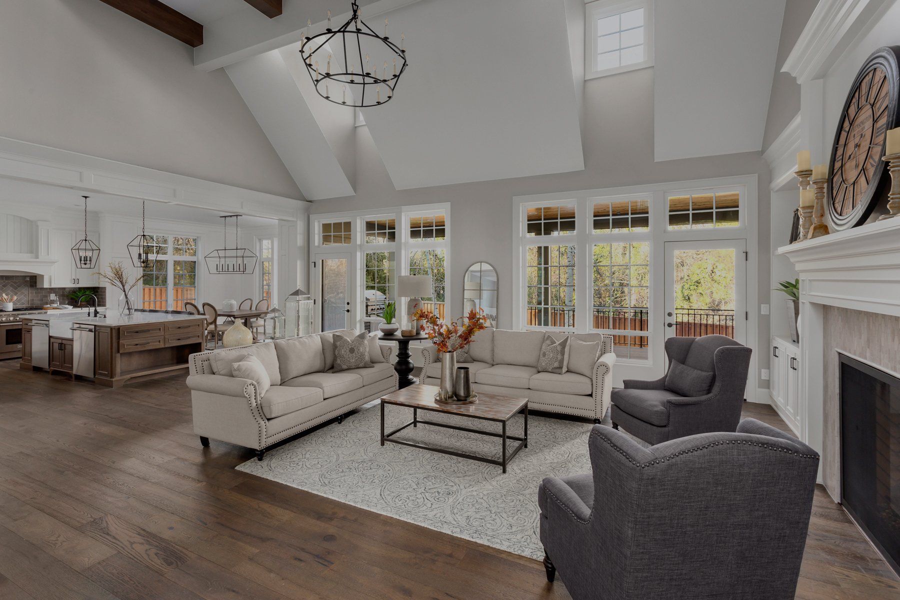 Bright living room with white sofas, gray chairs, coffee table, and tall windows with backyard view in Brookeville