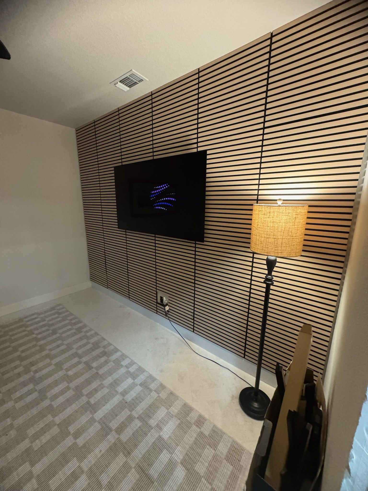 Hotel room with striped wall, wall-mounted TV, and a floor lamp beside a carpeted bed area