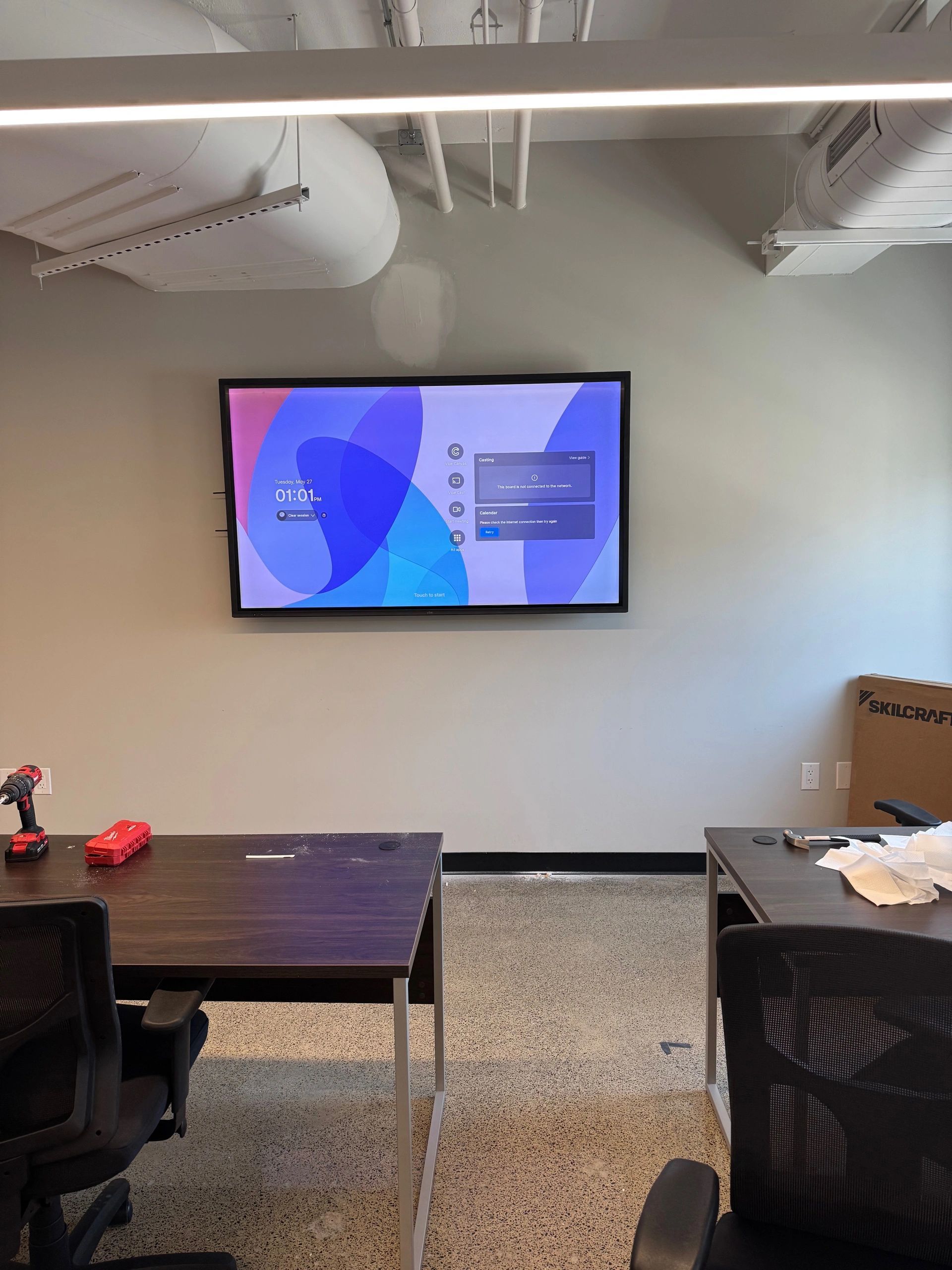 Conference room with wall-mounted presentation screen, dark table, and chairs on a speckled floor.