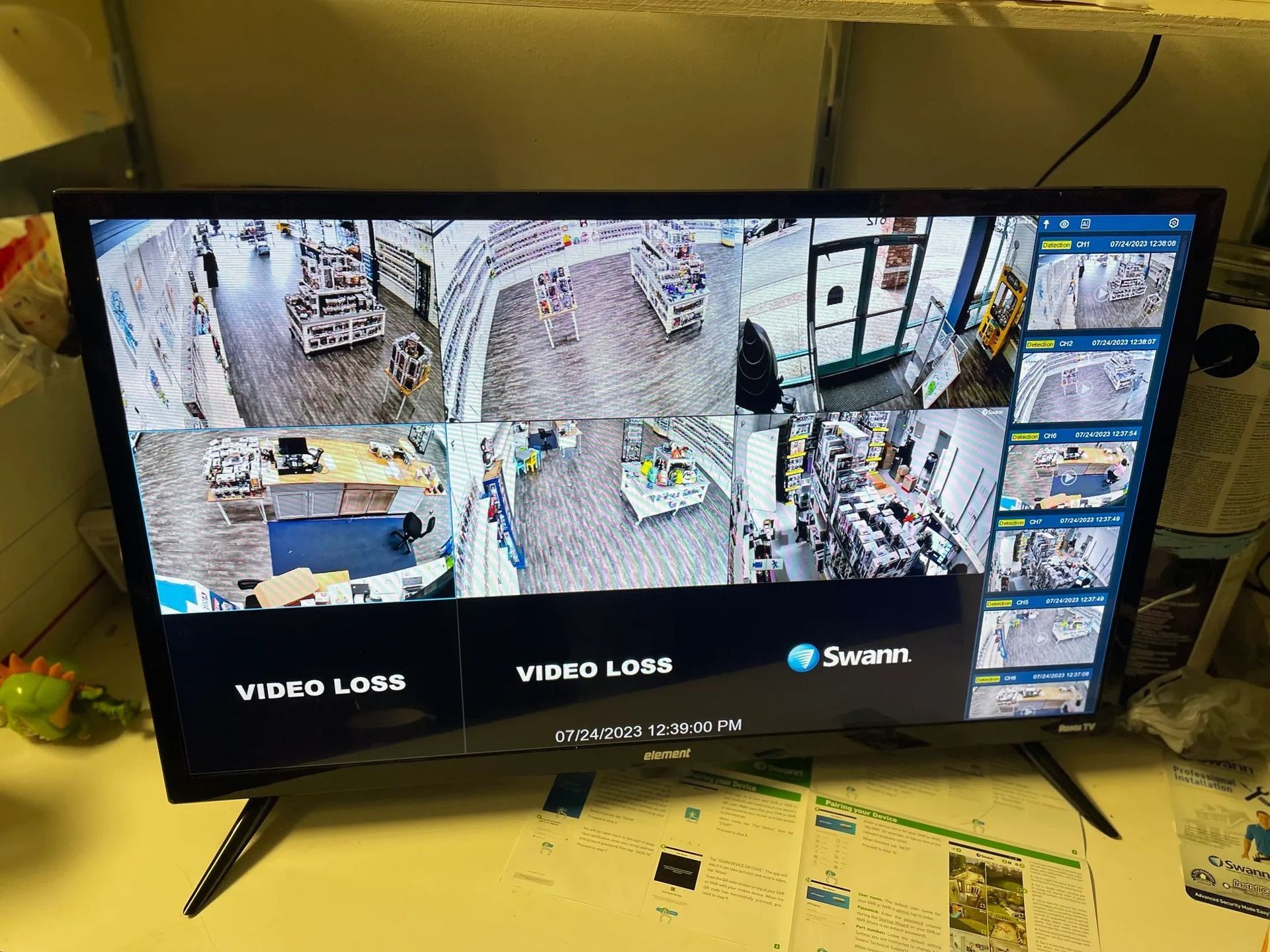 Security monitor showing multiple CCTV camera feeds in a control room, with a wall of surveillance screens.