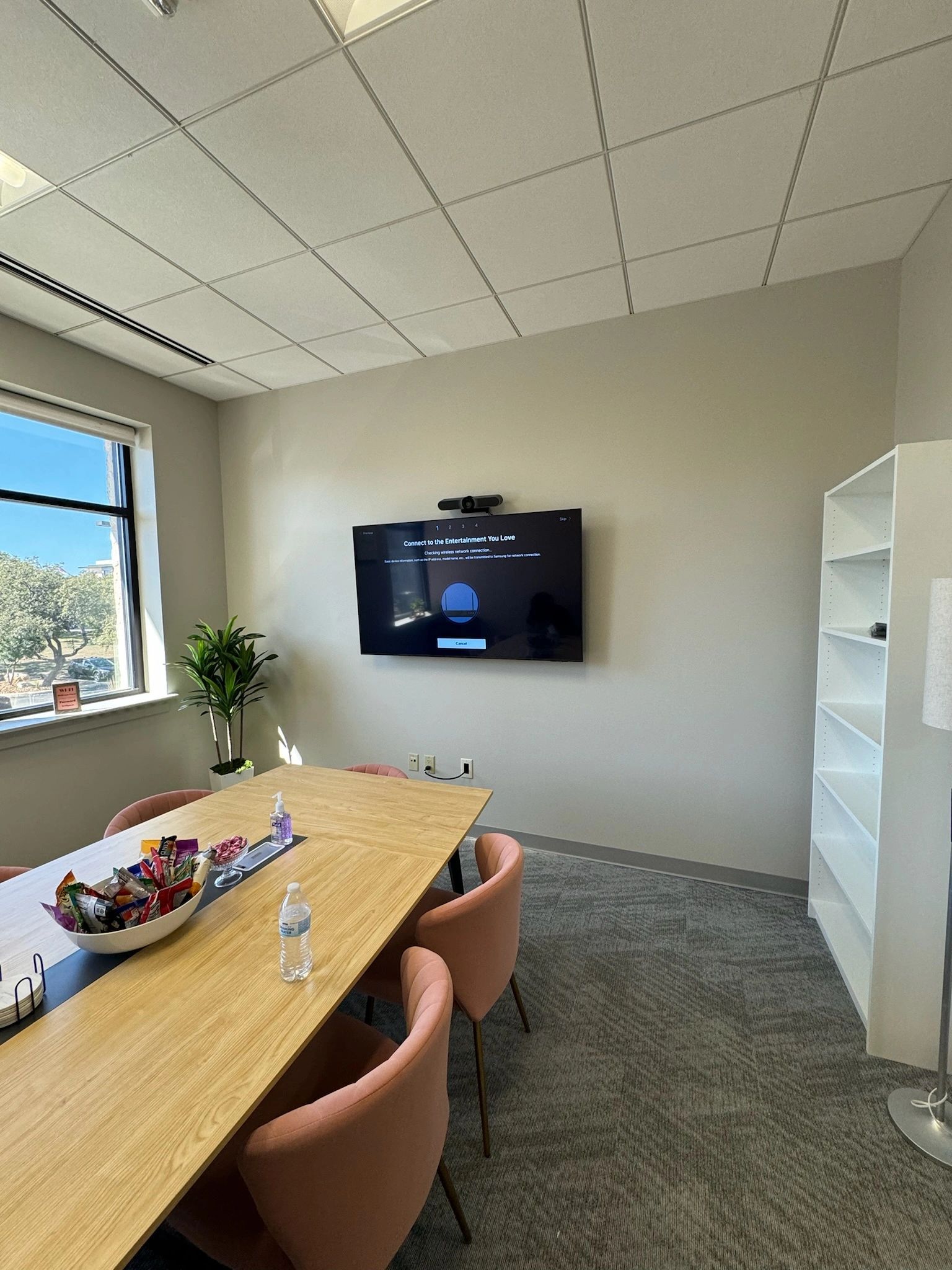 Modern conference room with wall-mounted TV, long table, chairs, and large window with city view