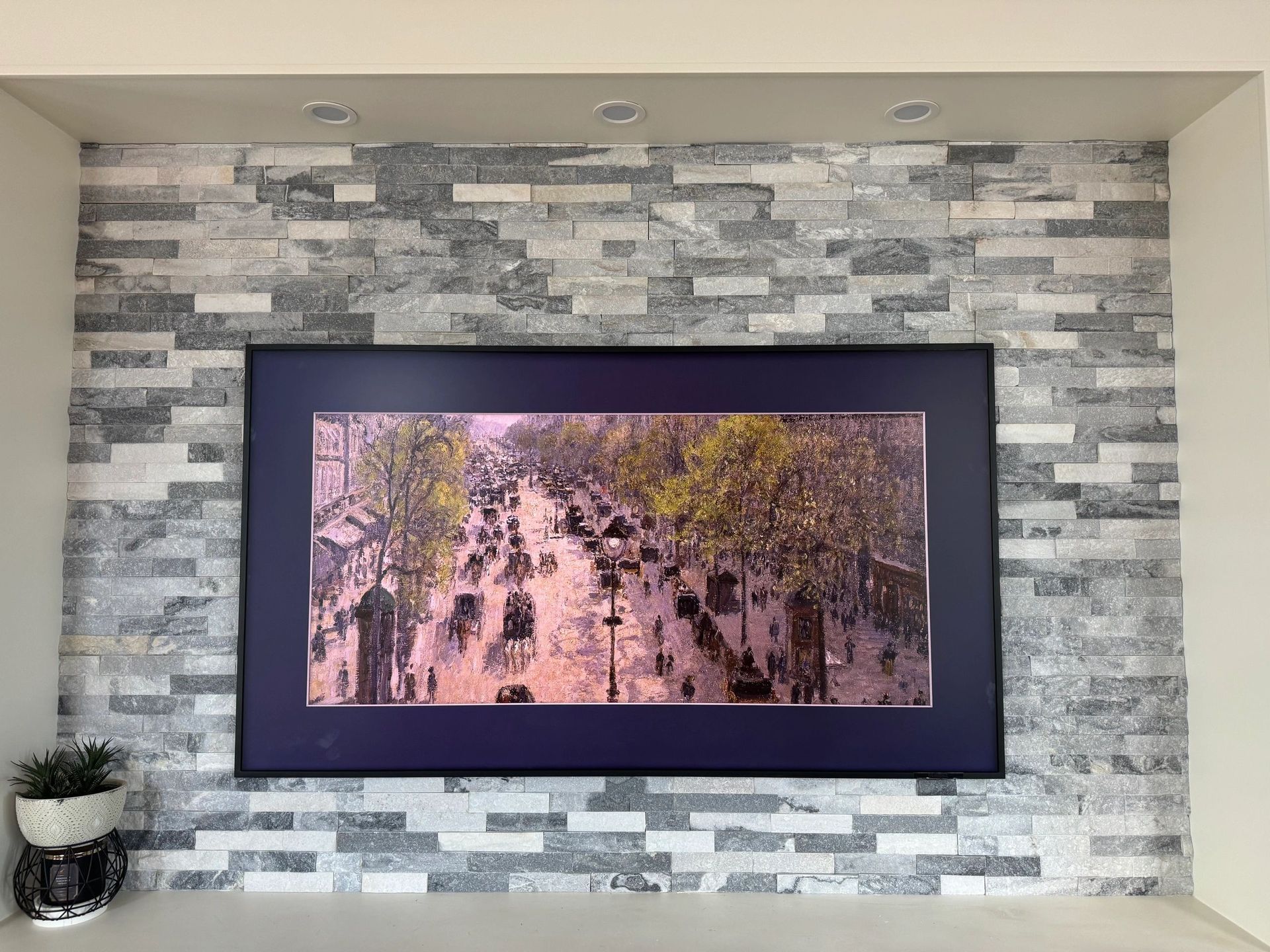 Framed landscape artwork with pink trees on a stone accent wall above a mantel