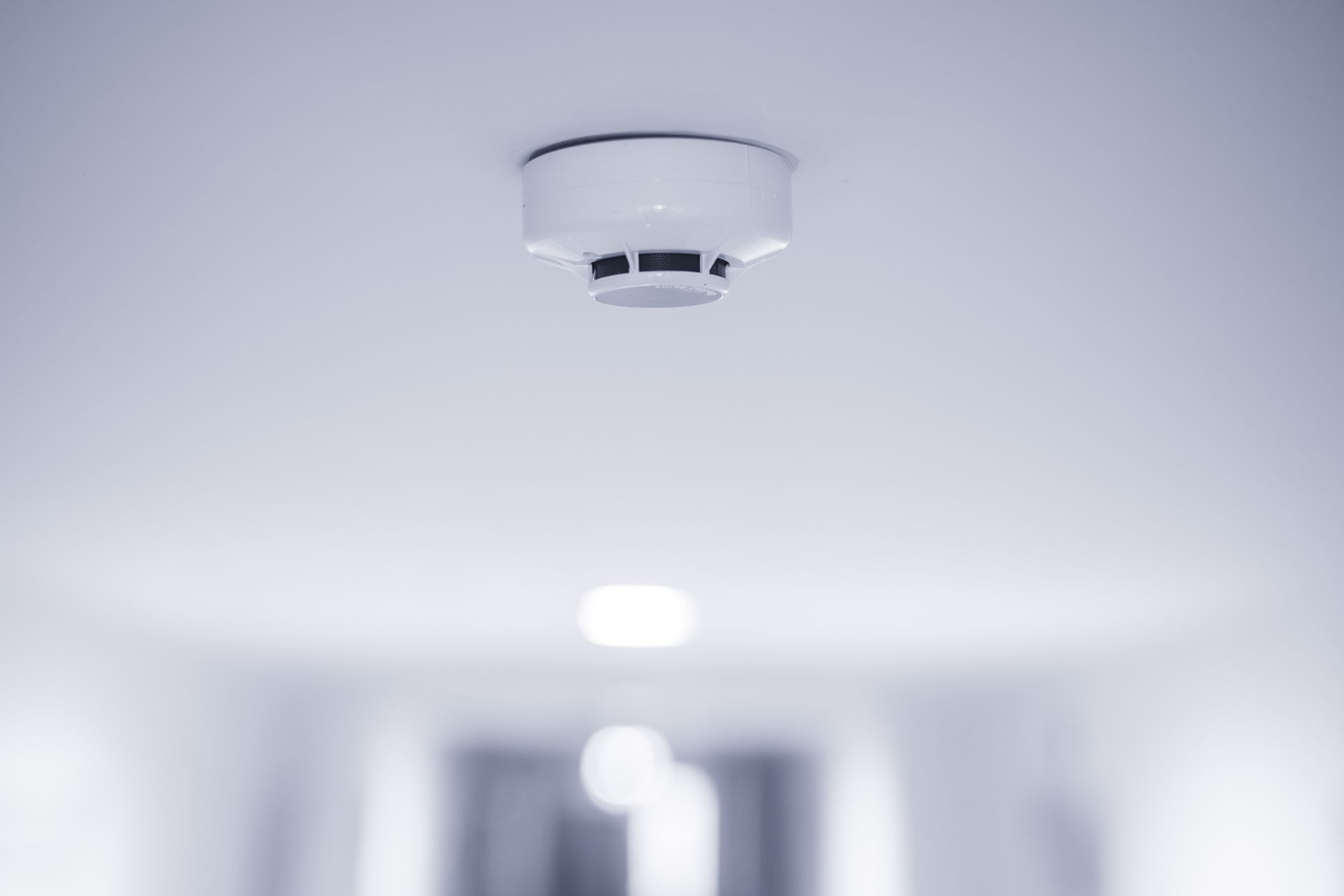 Ceiling-mounted smoke detector on a white ceiling in a hallway