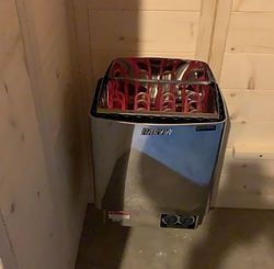 A stainless steel sauna heater is sitting in a corner of a room.