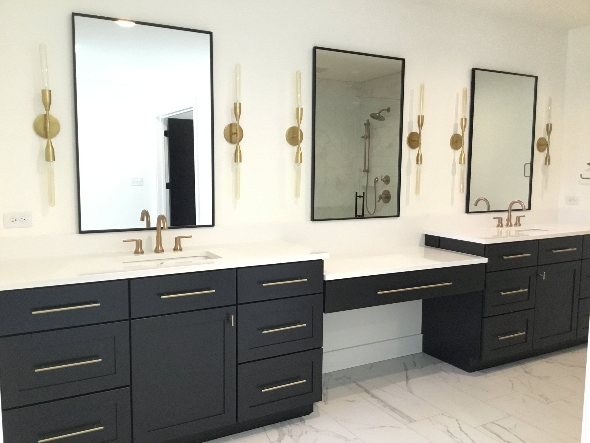 Modern bathroom with dark navy double vanity, three mirrors, brass sconces, and white tile floor.