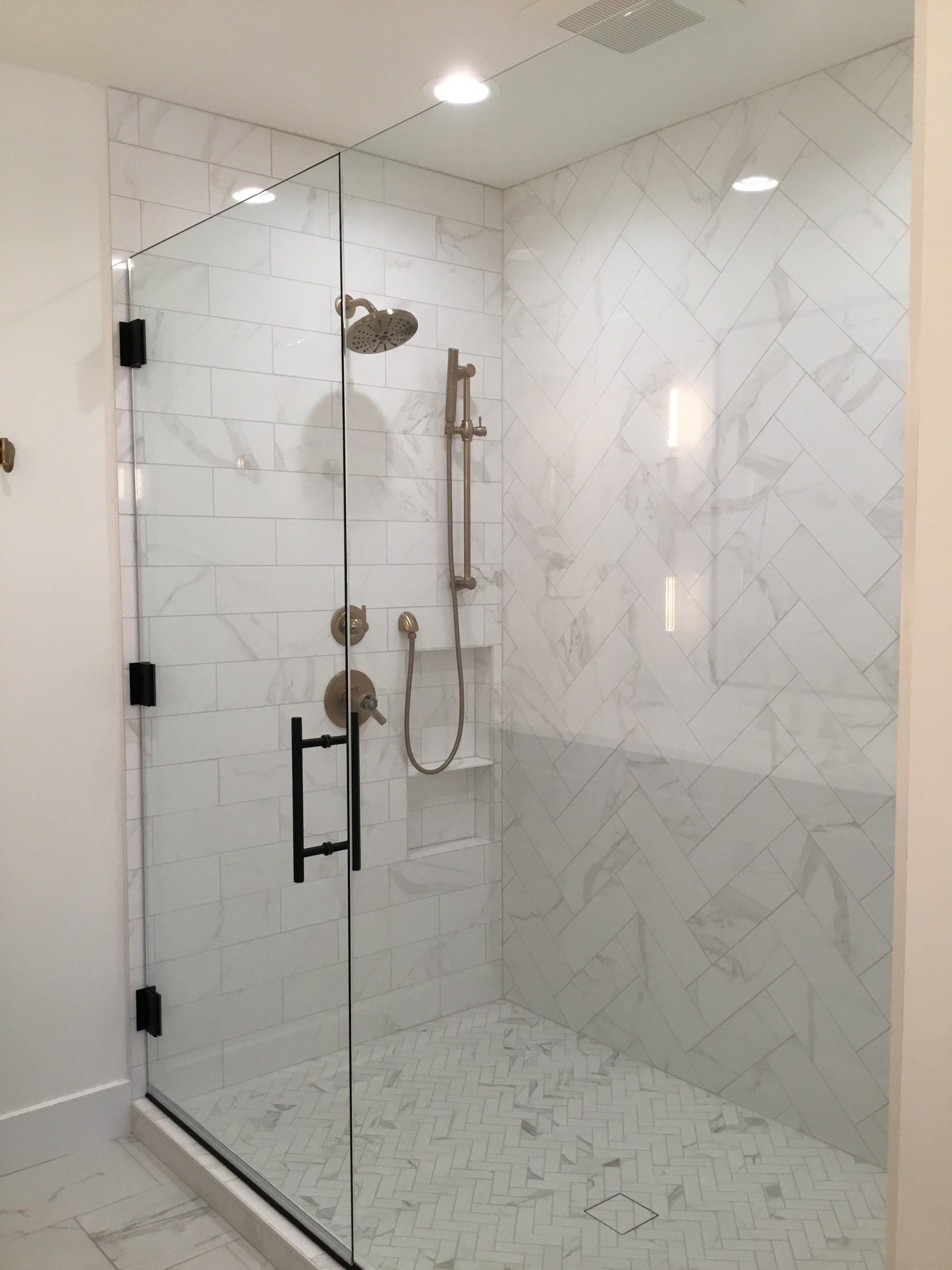 Modern glass shower with chrome fixtures in a white tiled bathroom.