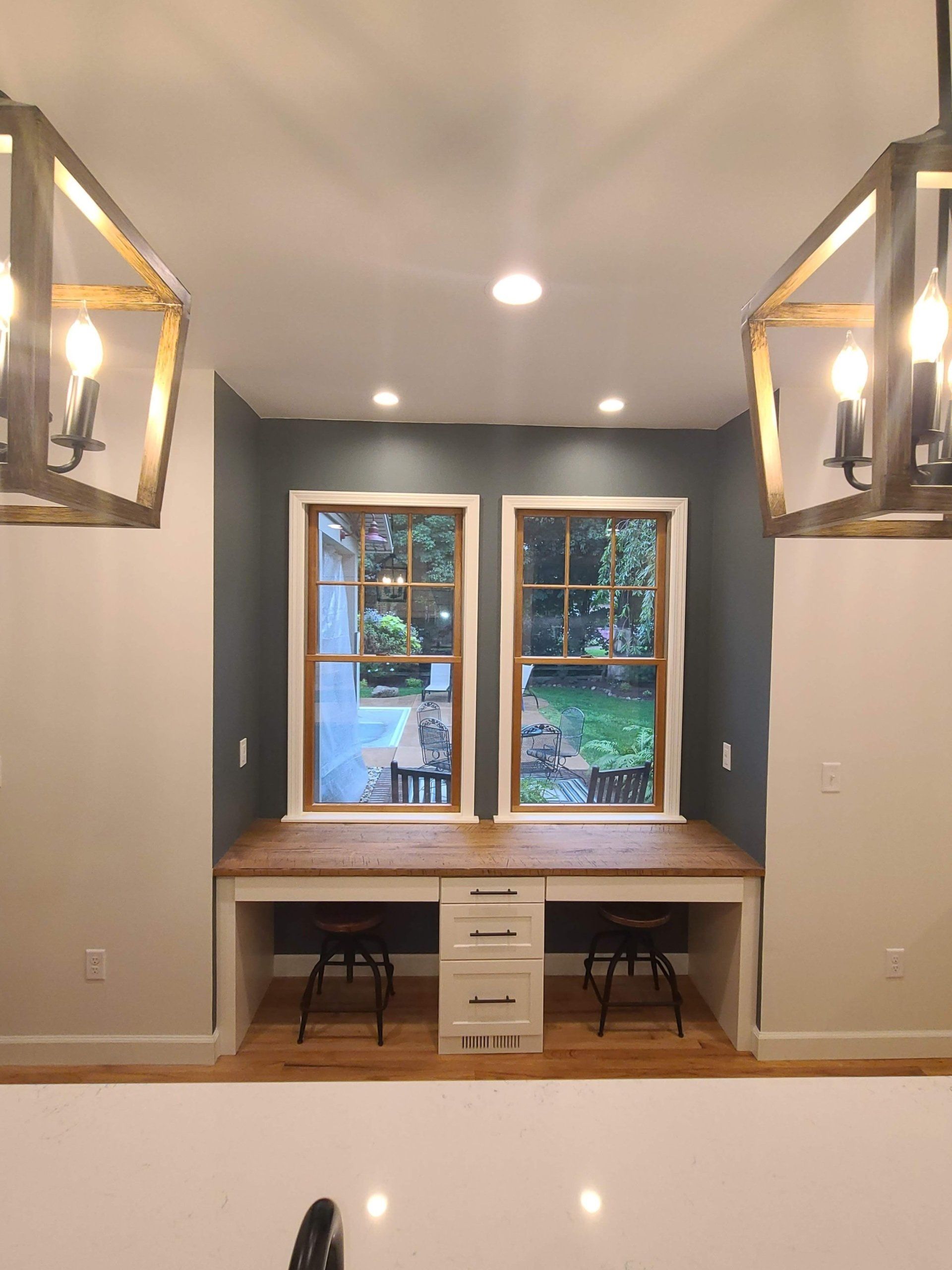 A kitchen with two desks and two windows.