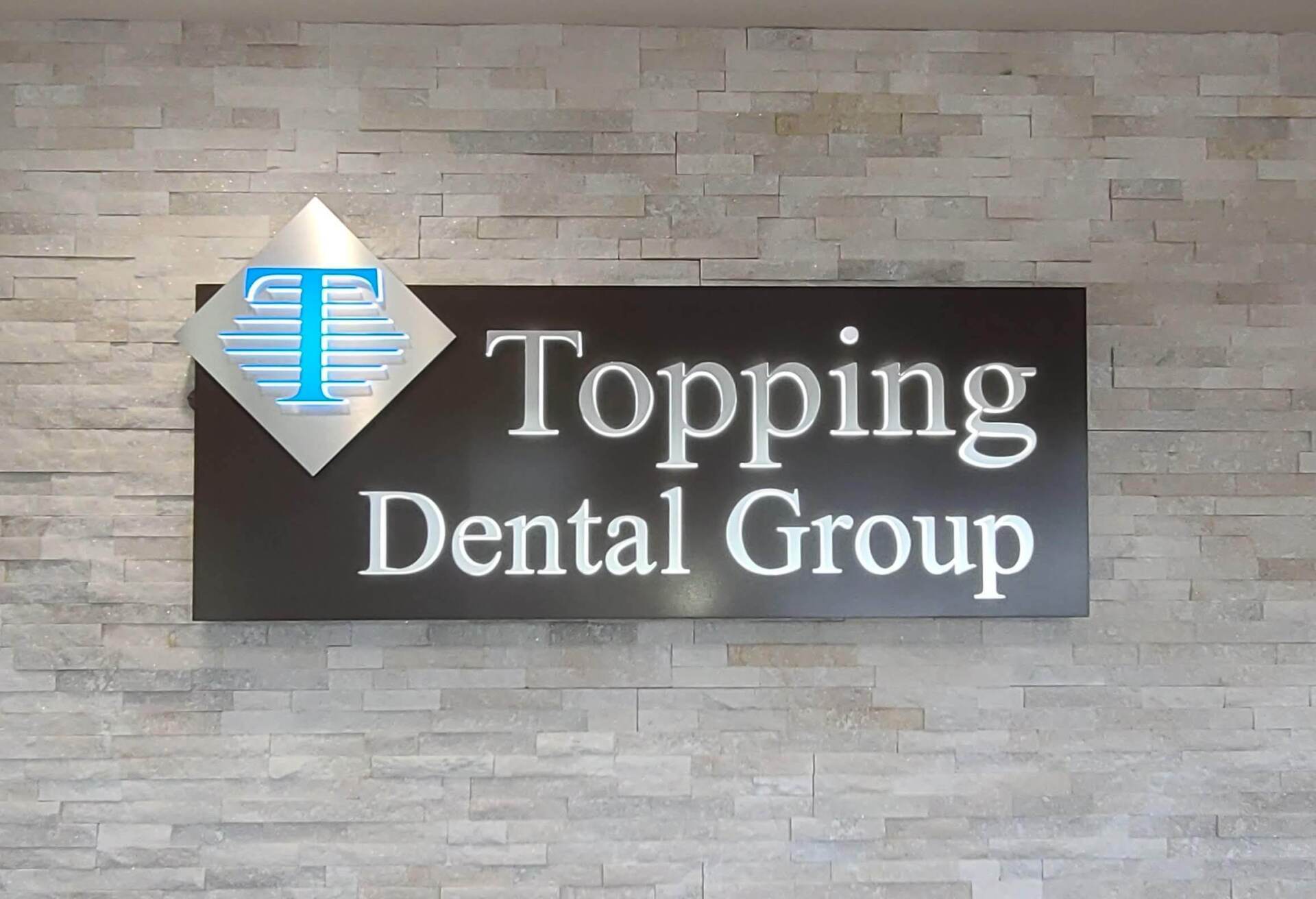 A sign for topping dental group hangs on a brick wall
