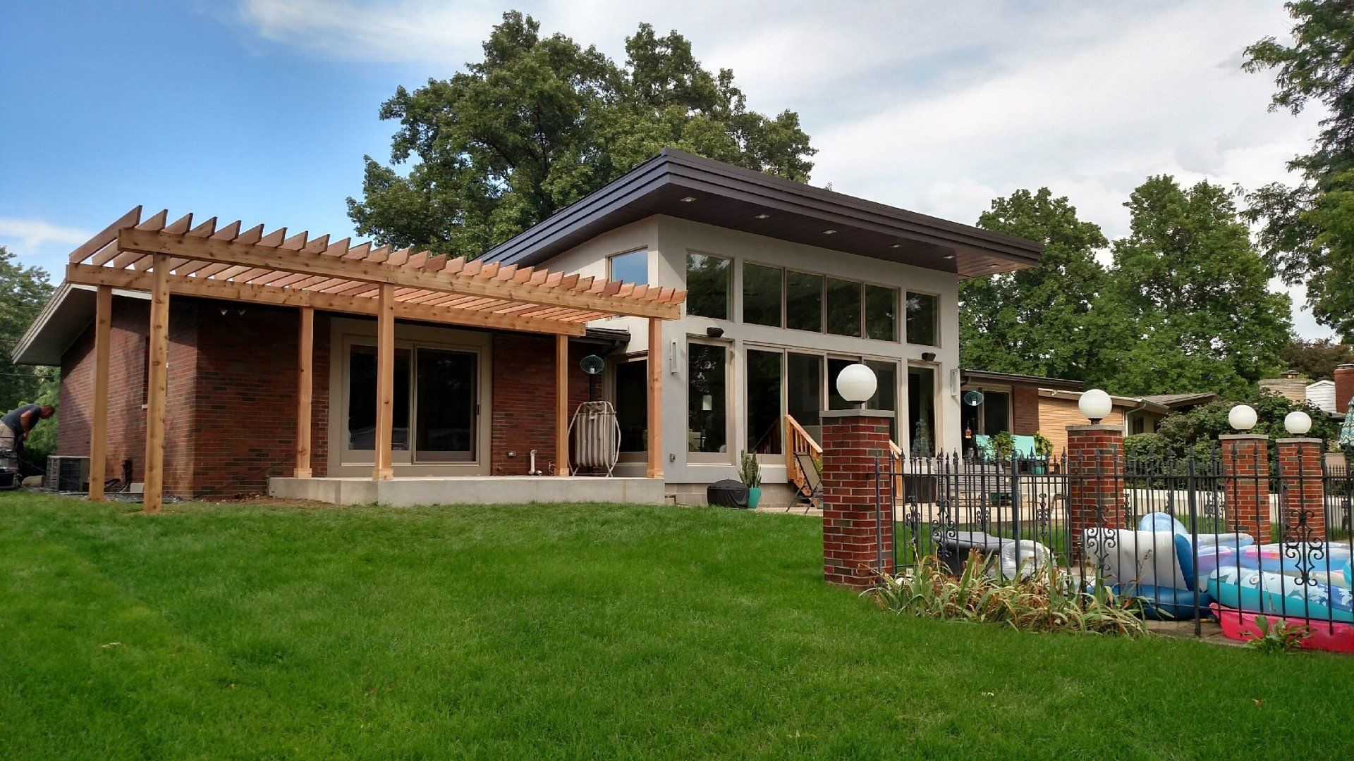 Backyard patio with a house, pergola, and swimming pool beside a green lawn