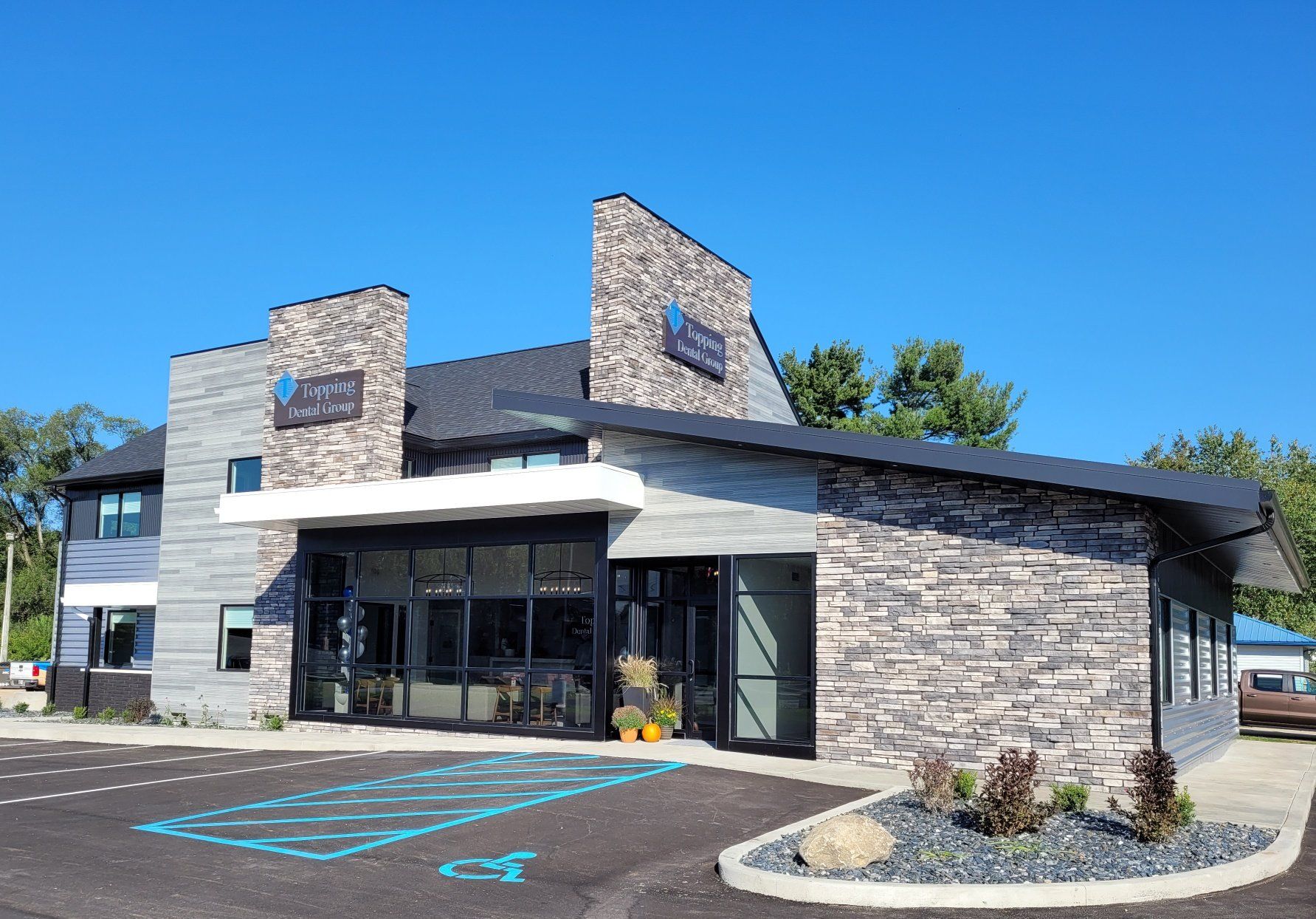 Modern stone-and-glass commercial building with parking lot and blue accessible spaces under a clear sky