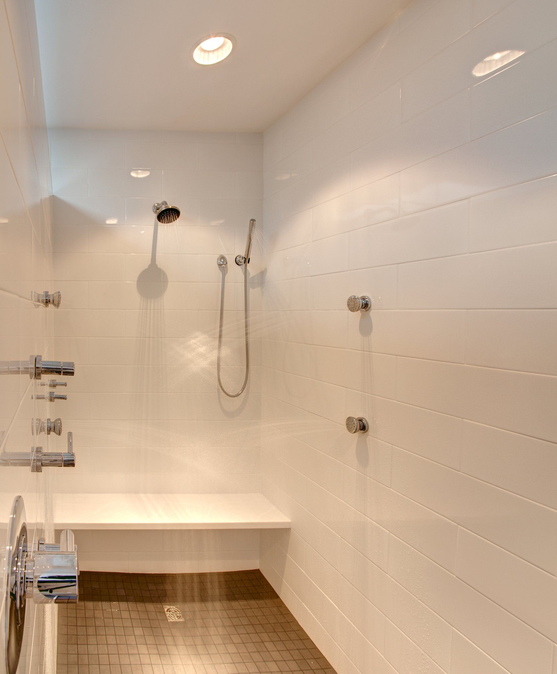 Modern white tiled shower with bench, handheld showerhead, and wooden floor trim