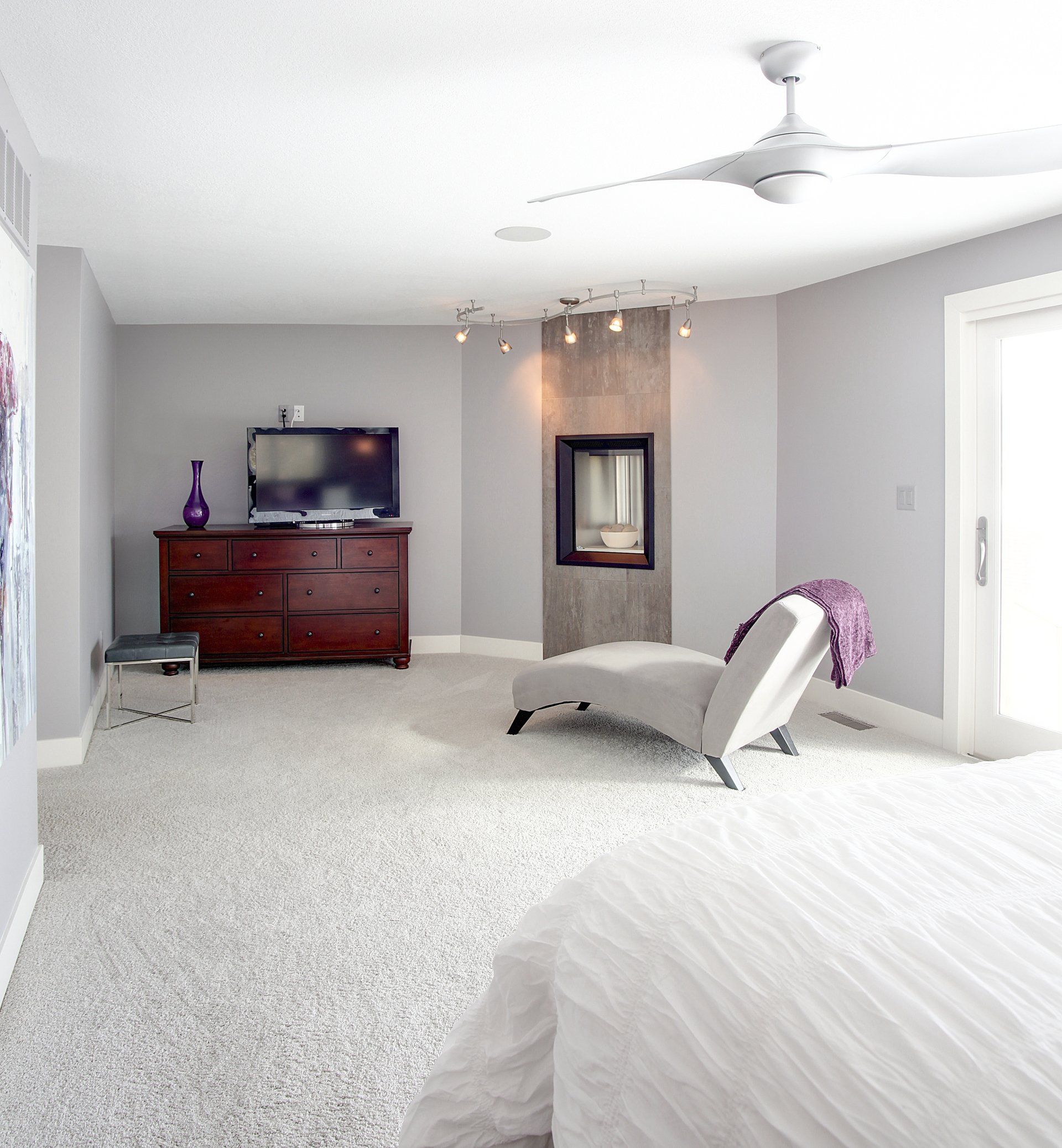 Bright gray bedroom with a dresser, wall mirror, chaise lounge, and ceiling fan.