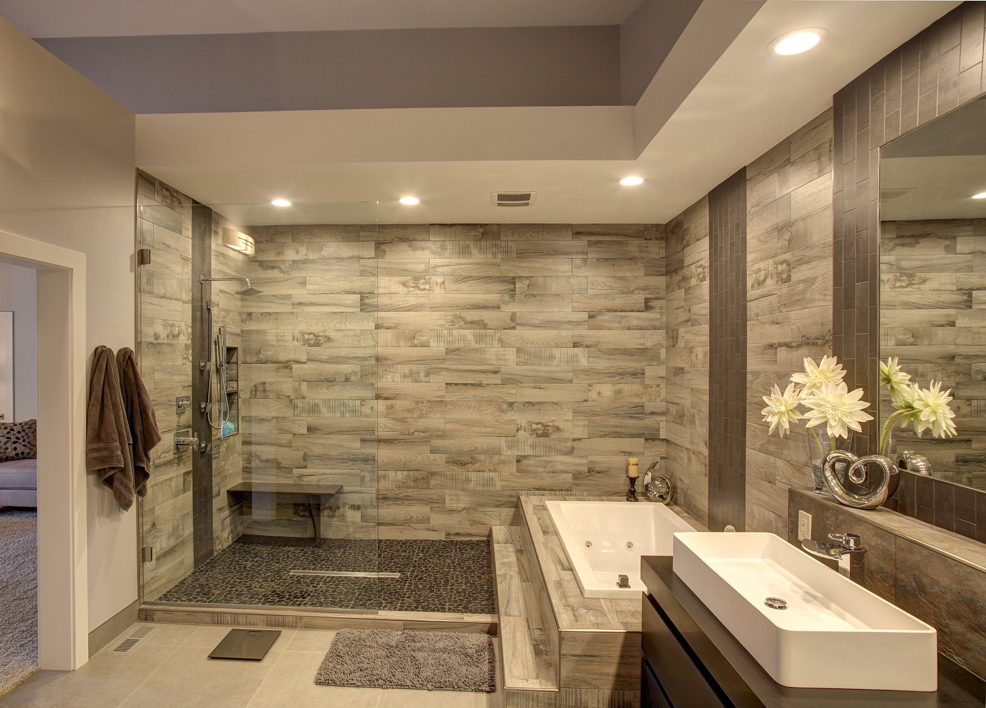 Modern bathroom with stone tile walls, double sink vanity, and a walk-in shower with bench