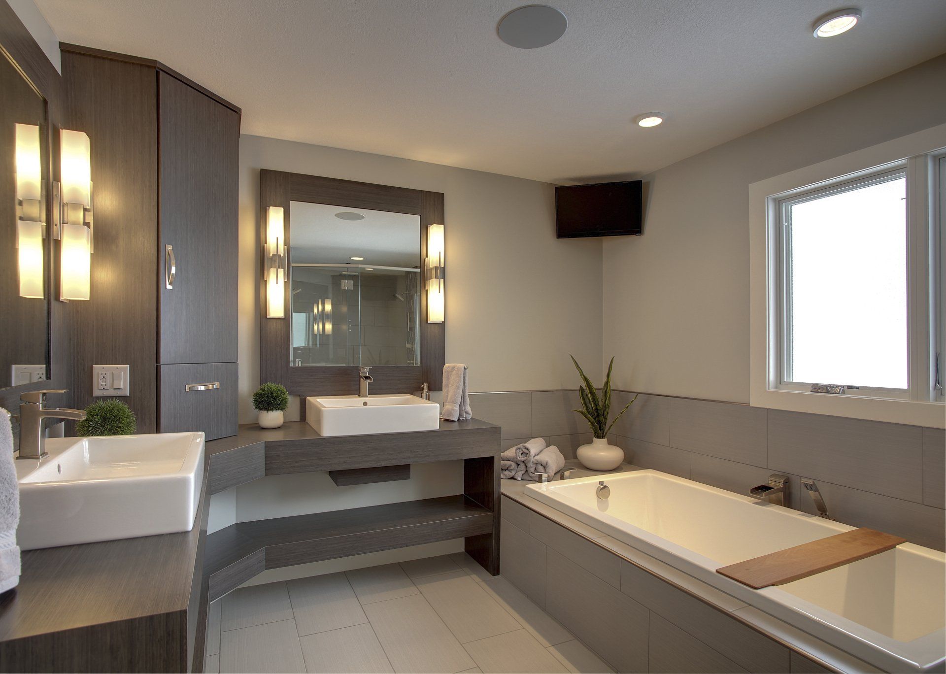 Modern bathroom with double vanity, large mirror, soaking tub, and gray tile walls and floor.