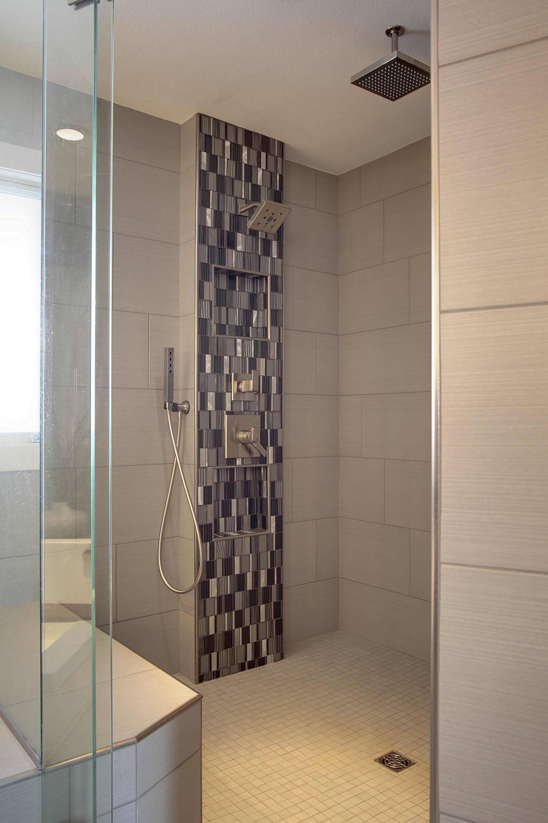 Modern tiled walk-in shower with glass door, rainfall showerhead, and mosaic accent strip