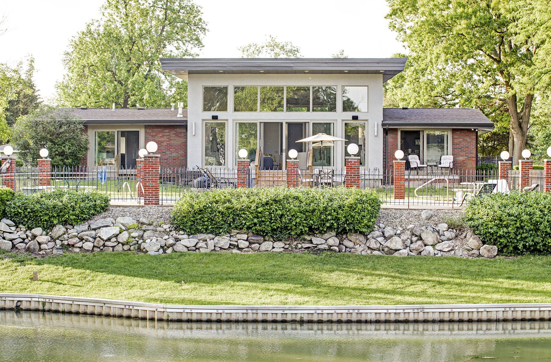 Lakeside building with red awnings, stone wall, and manicured garden reflecting in the water