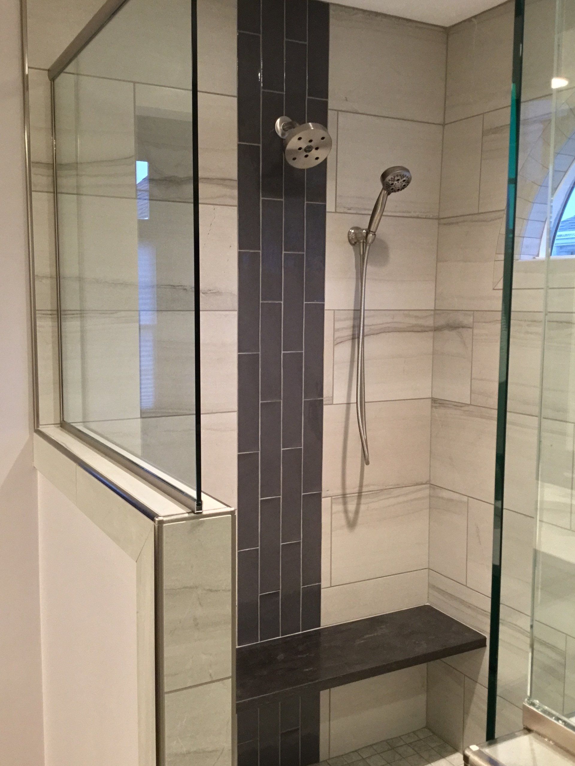 Glass-enclosed shower with dark accent tiles, a handheld showerhead, and a built-in bench.