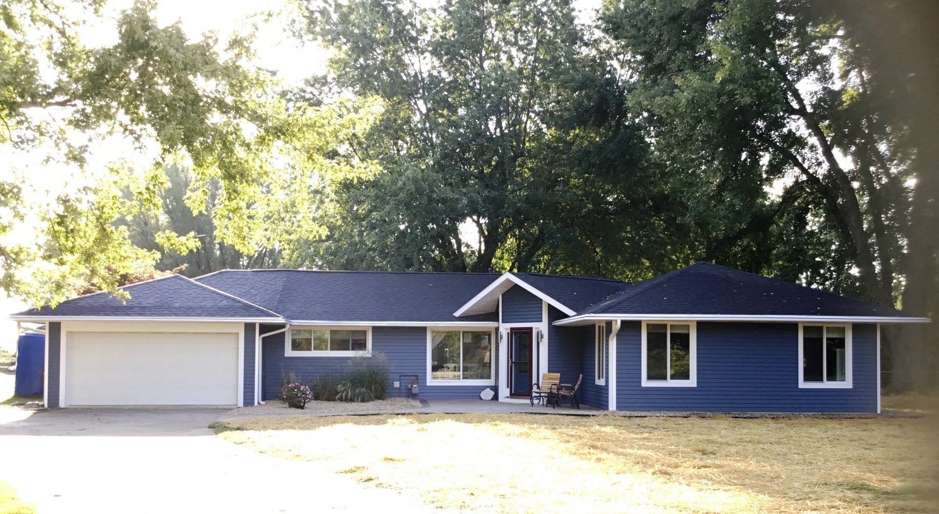 A blue house with a white garage door is surrounded by trees