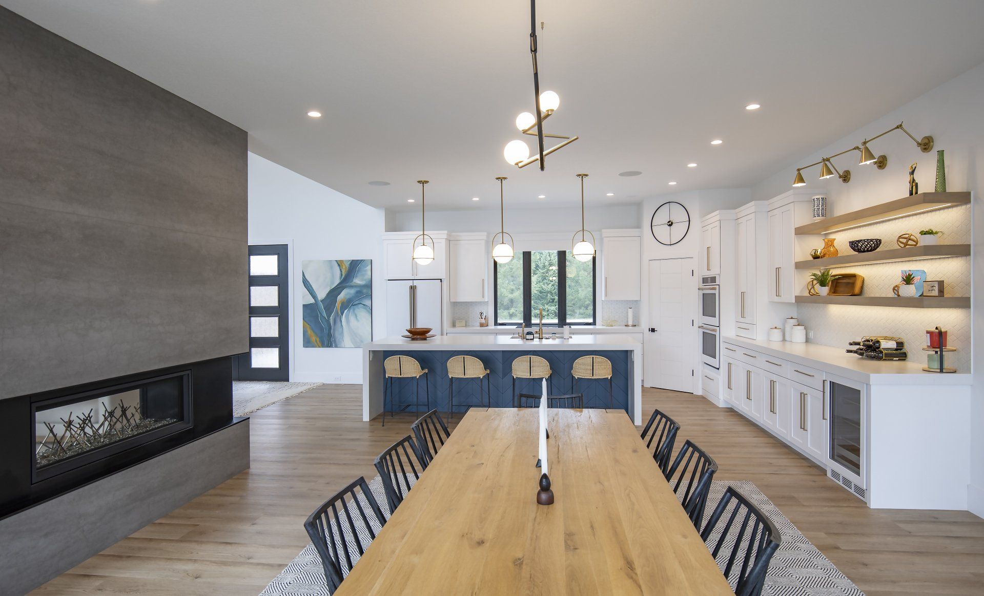 There is a long wooden table in the middle of the kitchen.