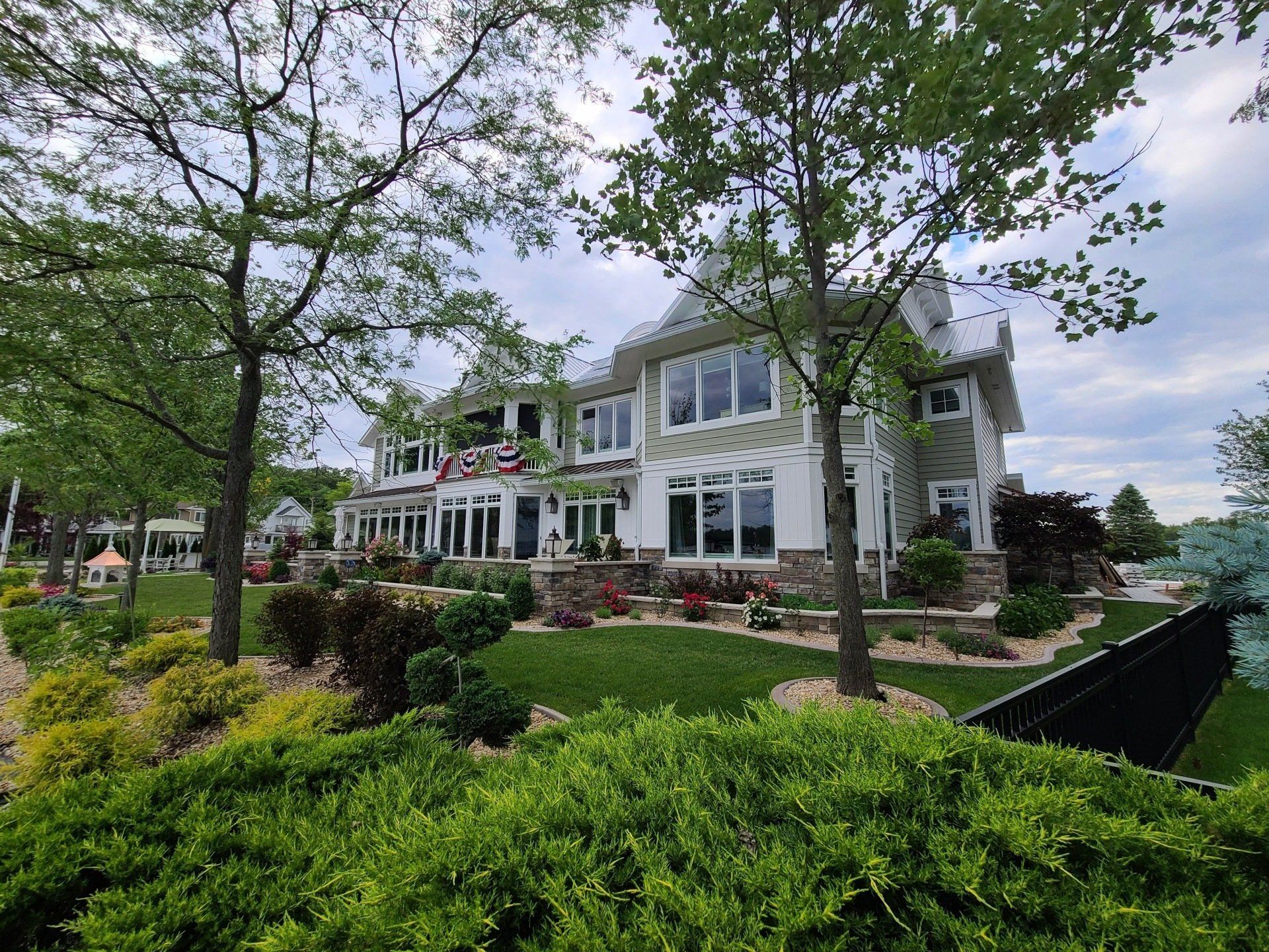 Large white waterfront house with a landscaped garden and trees under a cloudy sky