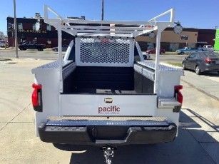 White utility truck bed with ladder rack and toolboxes parked in a lot, rear view