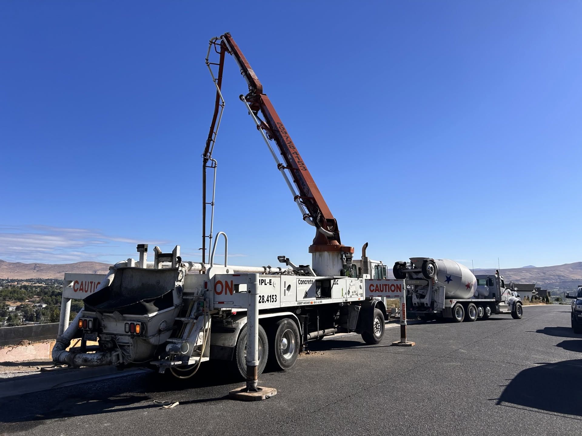 Concrete pump truck with extended boom pouring concrete into a mixer truck on a roadside worksite