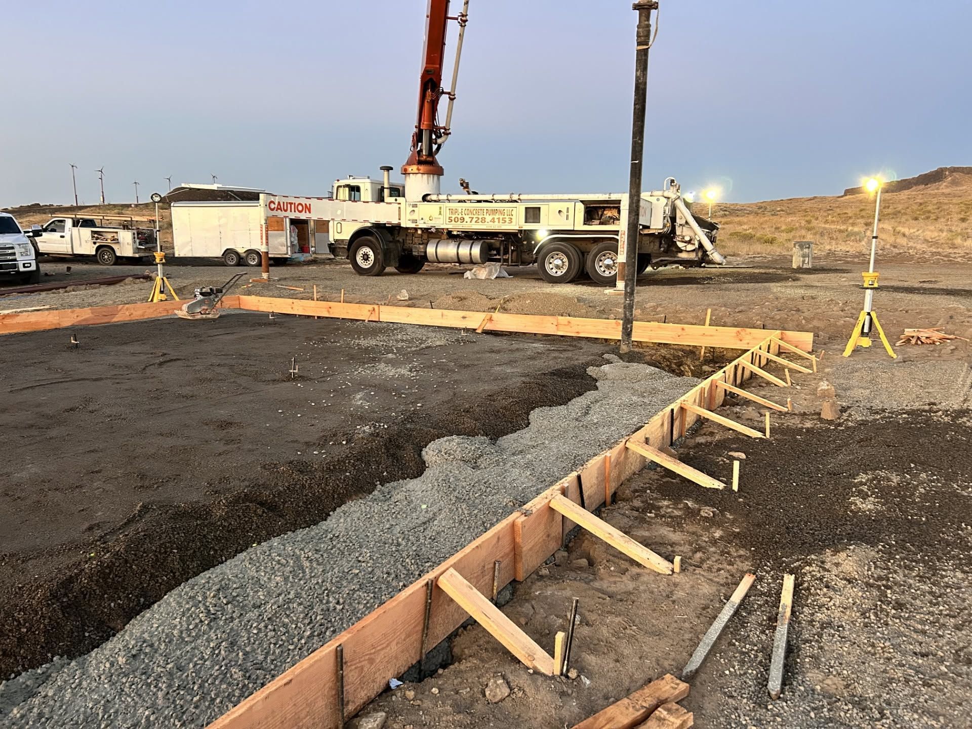 Concrete foundation forms at a construction site with trucks, equipment, and dirt ground under a clear sky
