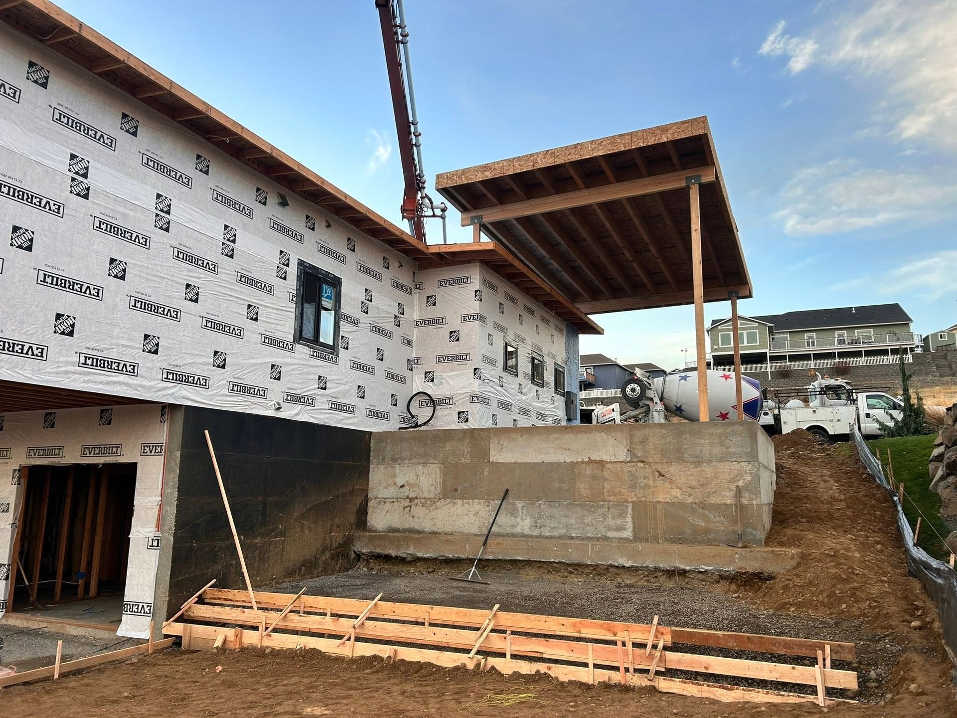 Partially built house exterior with white siding, concrete foundation, and a covered porch under construction