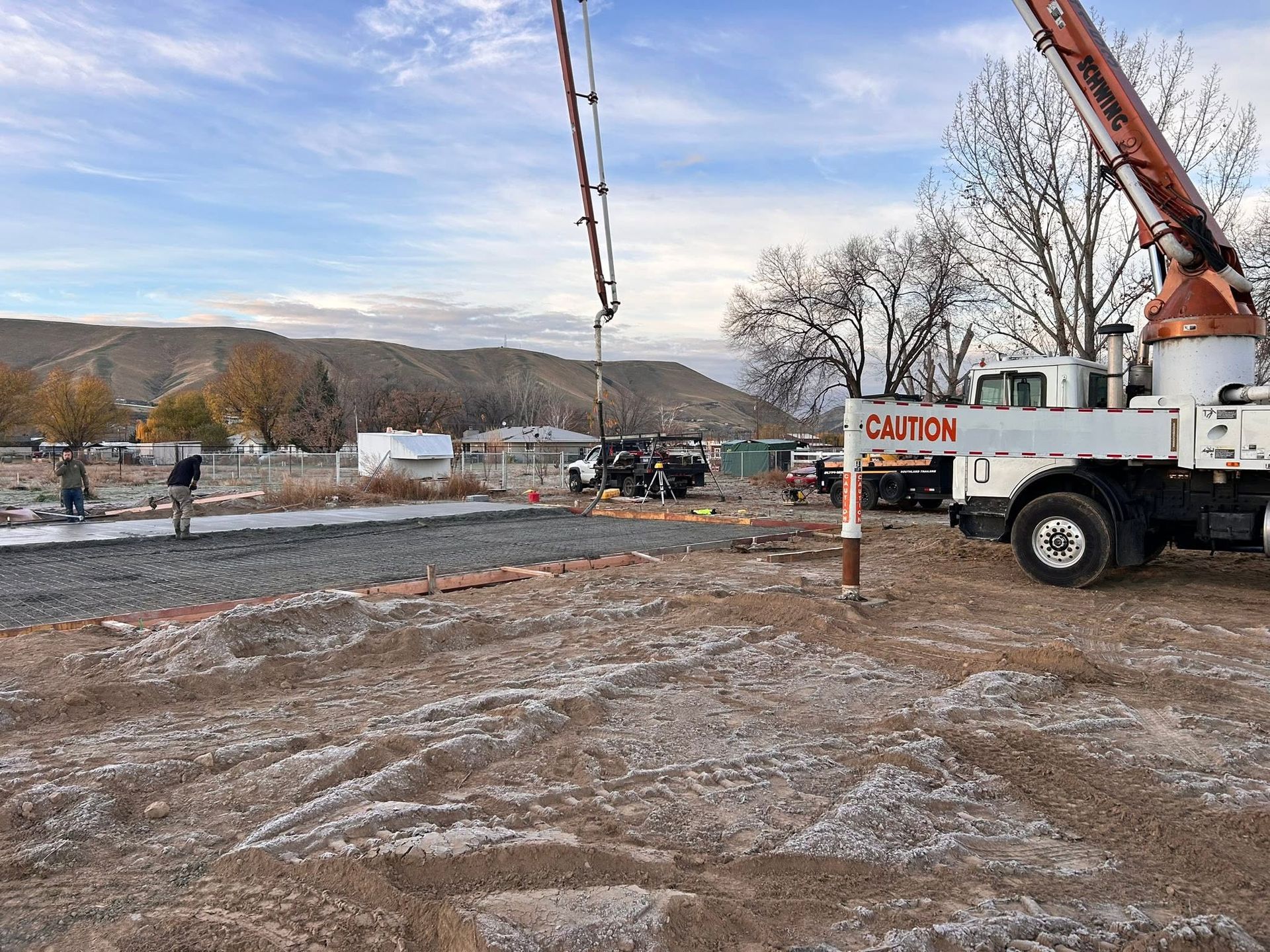 Crane truck at a muddy construction site with utility poles and a small building in the background